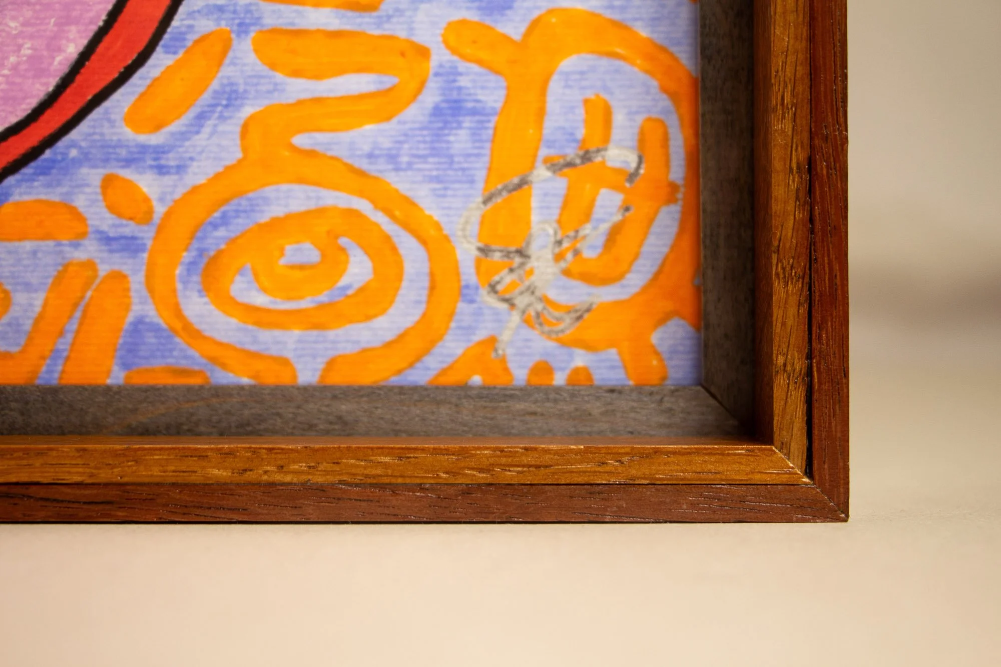 Unseen Signifiers 010 frame detail: close-up through the acrylic of the lower right corner, showing the silver signature over the pale blue field with orange symbols, bordered by the dark inner liner and warm wooden frame. mahogany, oak and beech woo