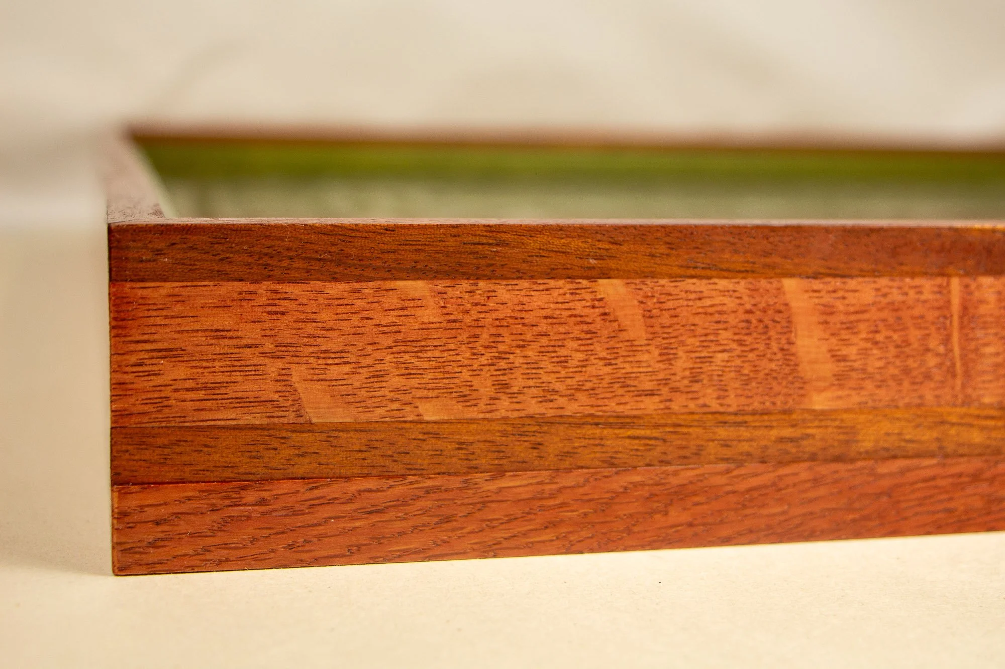 Close-up of a wooden art frame with a smooth surface and visible wood grain, with a green spacer, set against a beige background.