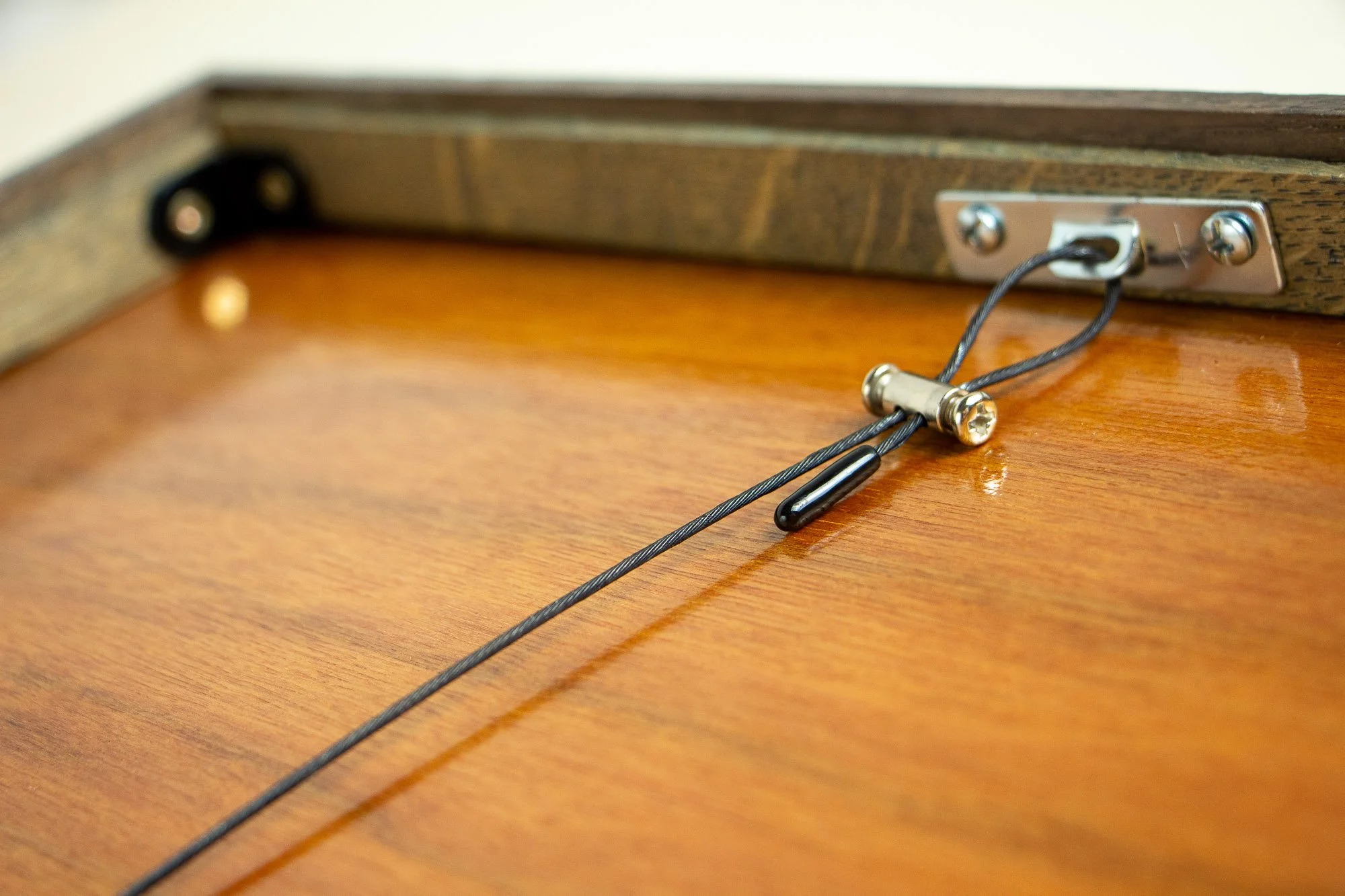 Luminous Parallax 003 frame: reverse hardware detail showing the hanging cable, metal anchor plate, screws, and the polished wood back panel within the dark outer rim.