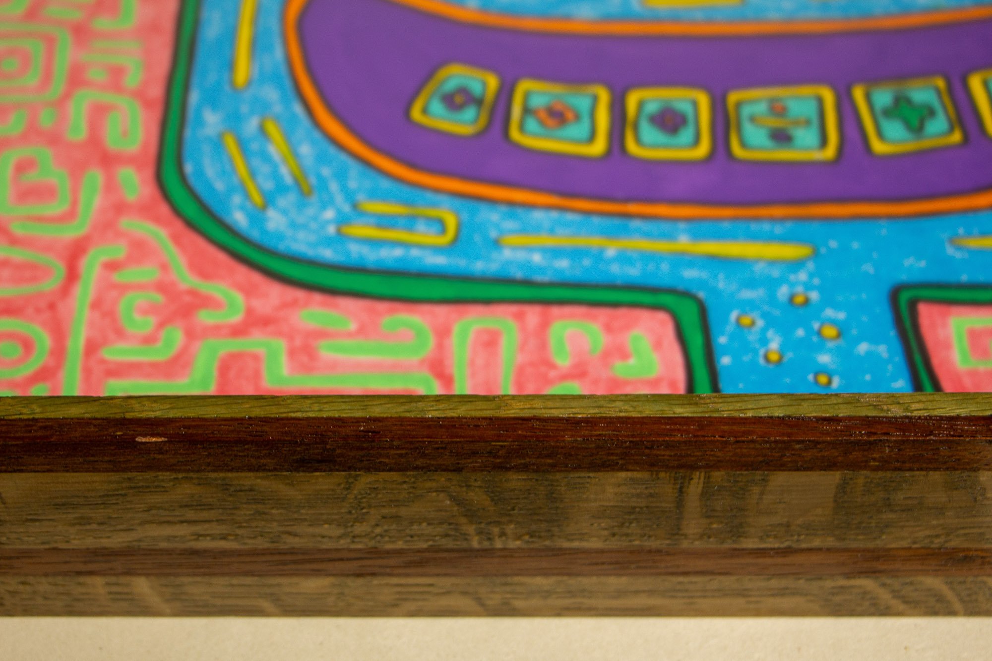 Unseen Signifiers 001 frame detail: horizontal close-up of the lower frame edge, with the layered wood profile in the foreground and the artwork’s pink, blue, yellow, and purple forms softly visible above it. mahogany, oak and beech wood.