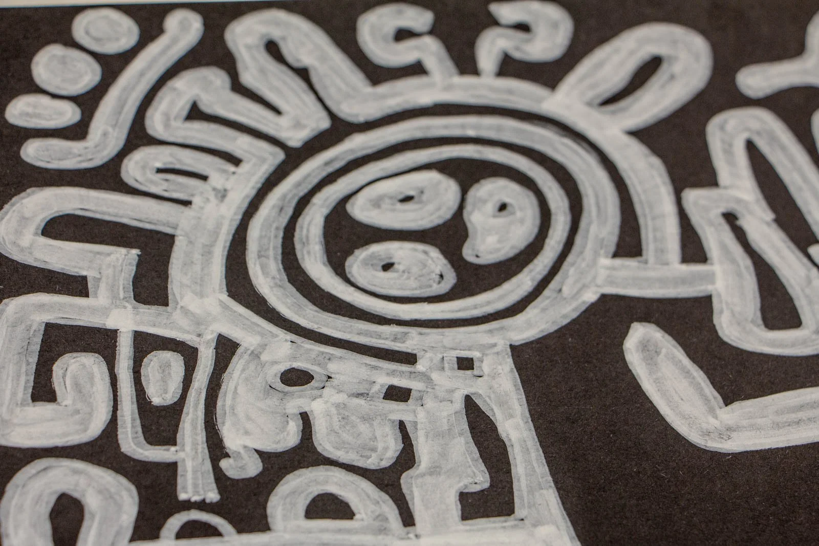 Metamorphic Entwining 004 detail: rosette/sun emblem with three inner dots; concentric rings and short radiating ticks intersect a figure-line