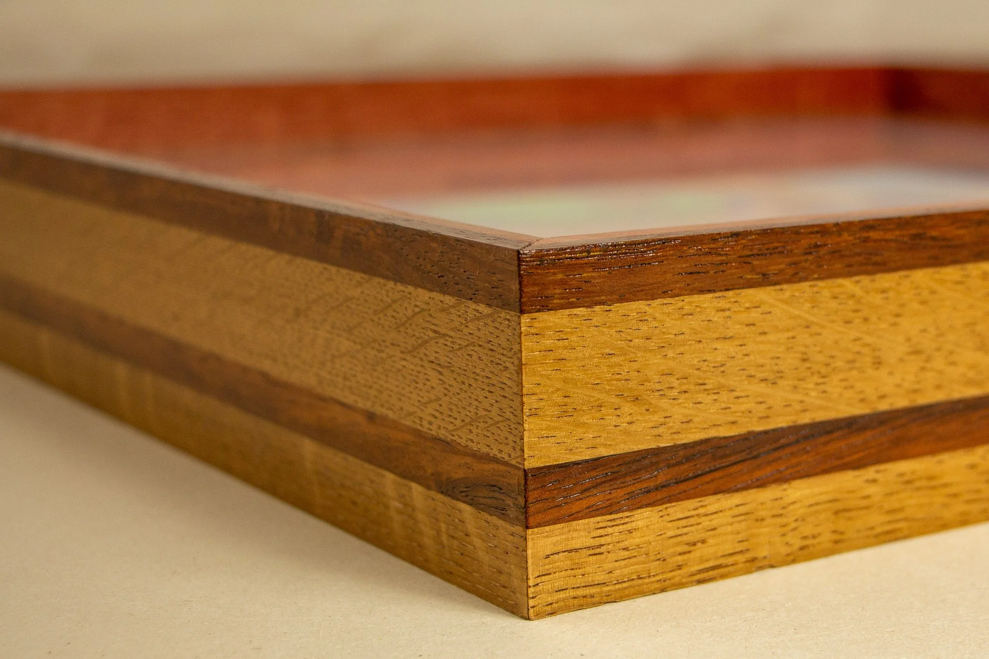 Unseen Signifiers 004 frame detail: corner close-up of the side profile, showing a layered warm wood frame with a dark reddish top edge, lighter honey-toned bands, and a narrower reddish strip running through the middle. mahogany, oak and beech wood.