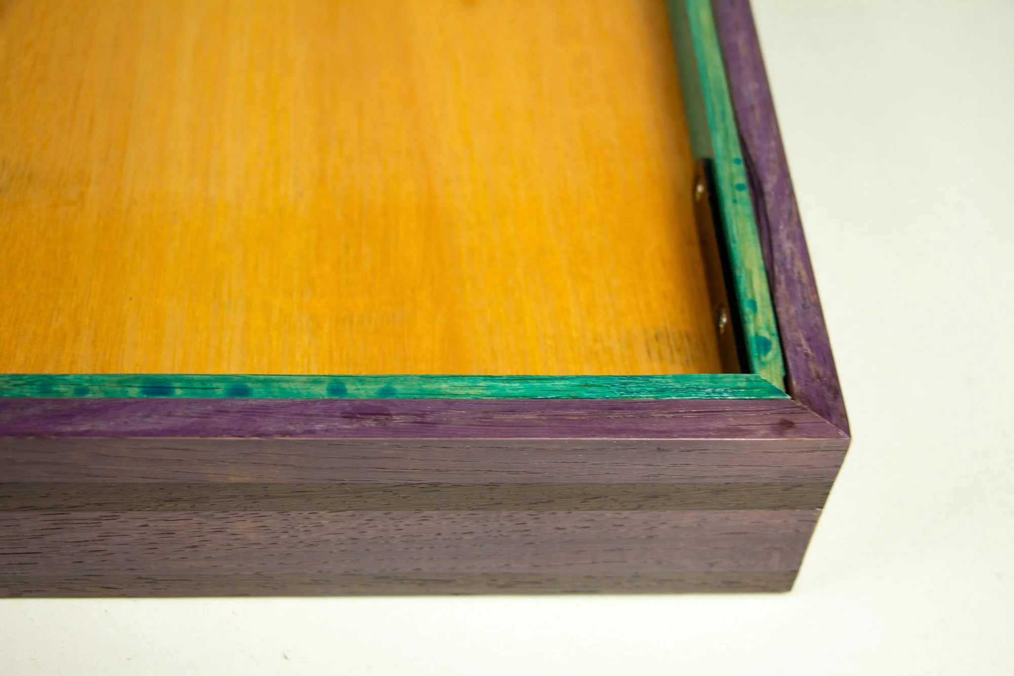 008; Elusive Cocoon 003 frame: reverse-side corner detail with meranti plywood back panel, mint-toned inner rim, violet-toned outer band, and a black corner bracket fixed into the frame construction.