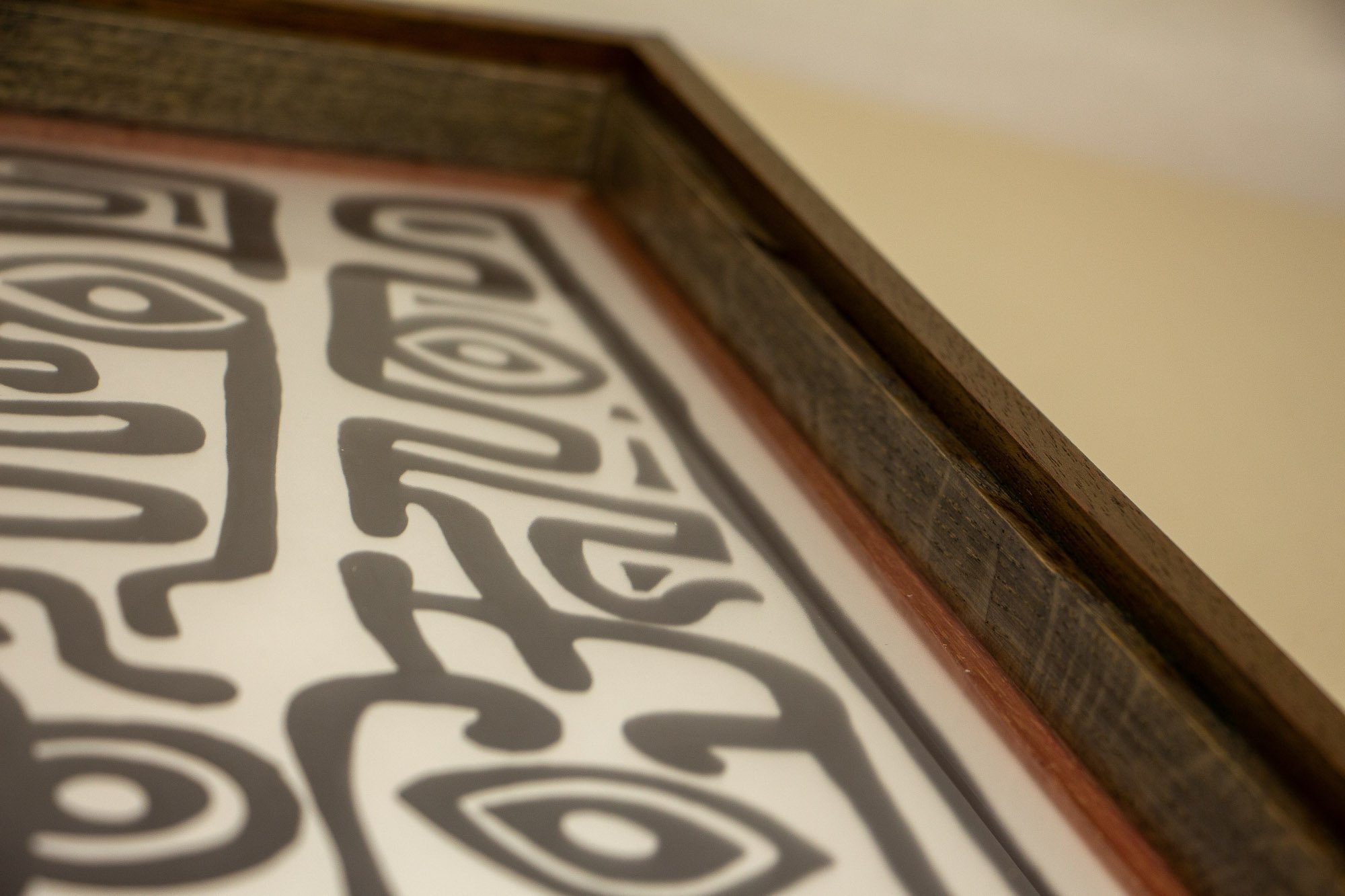 Resonant Syntax 004 frame: angled inside-corner detail of the frame, showing the layered construction, dark inner oak band, red inner lip, and the artwork surface below the glass