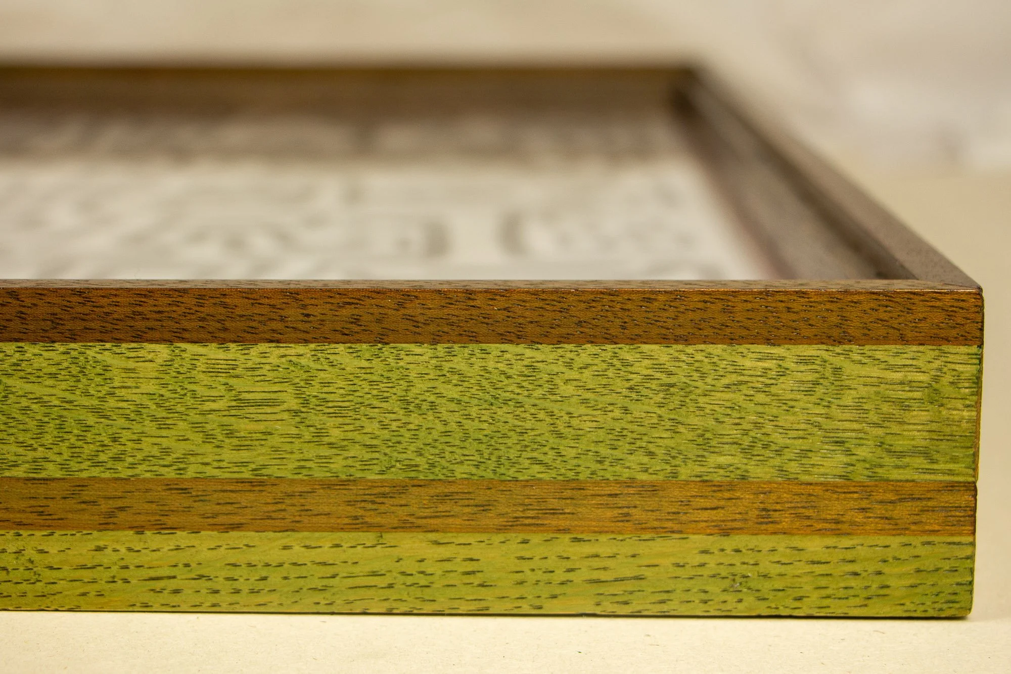 Resonant Syntax 004 frame: frontal edge detail of the frame profile, with alternating green and warmer granada-red bands, visible wood grain, and a clean finished outer edge