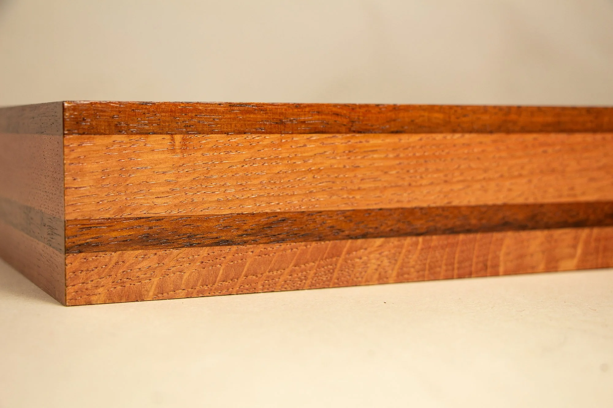 Unseen Signifiers 010 frame detail: angled side view of the layered wooden frame, showing warm honey-brown tones, a darker central stripe, and the refined horizontal banding of the grain. mahogany, oak and beech wood.