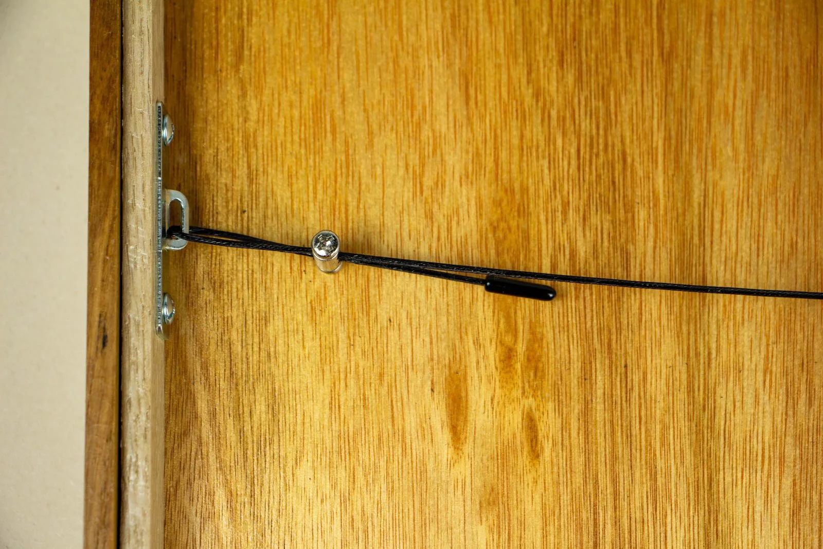 Golden Nostalgia 003 frame: rear hardware, black safety cable with nickel ferrule; anchored to a steel plate on the oak back panel