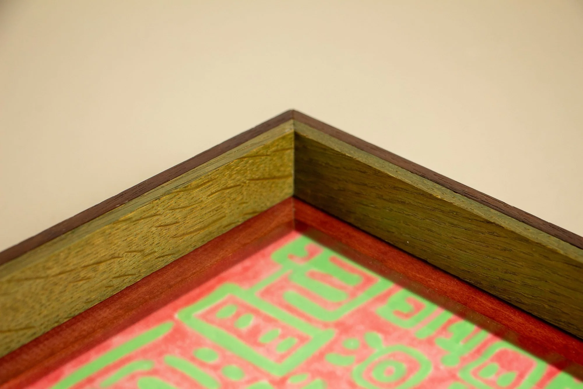 Unseen Signifiers 001 frame detail: mitered top-corner view of the frame, showing the angled join between the olive outer band, the dark upper edge, and the warm reddish inner strip around the artwork. mahogany, oak and beech wood.