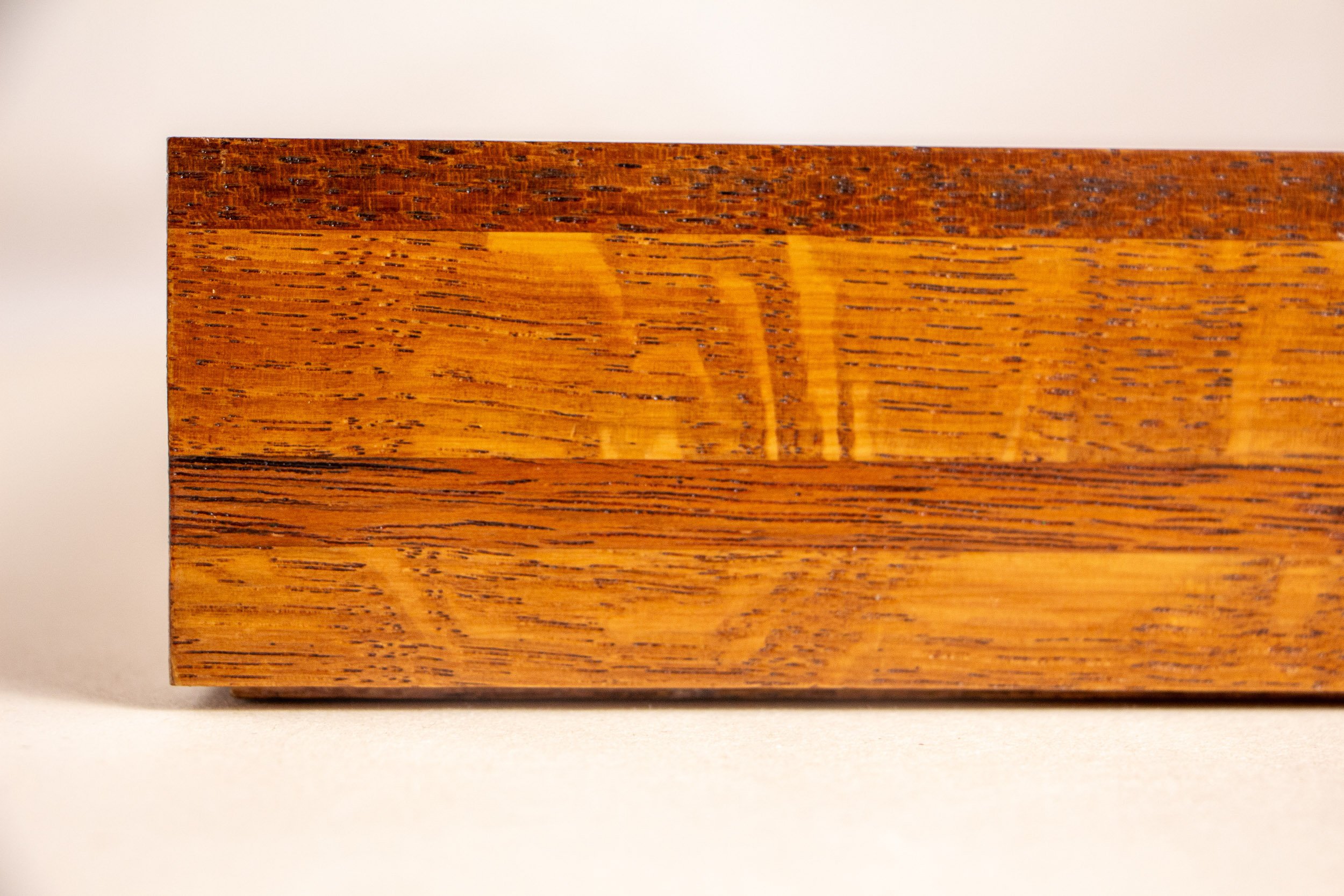 Turbulent Aegis 003 frame detail: close-up of the handcrafted frame corner, showing the layered wood construction, rich amber-brown tones, visible grain, and polished lacquered finish.