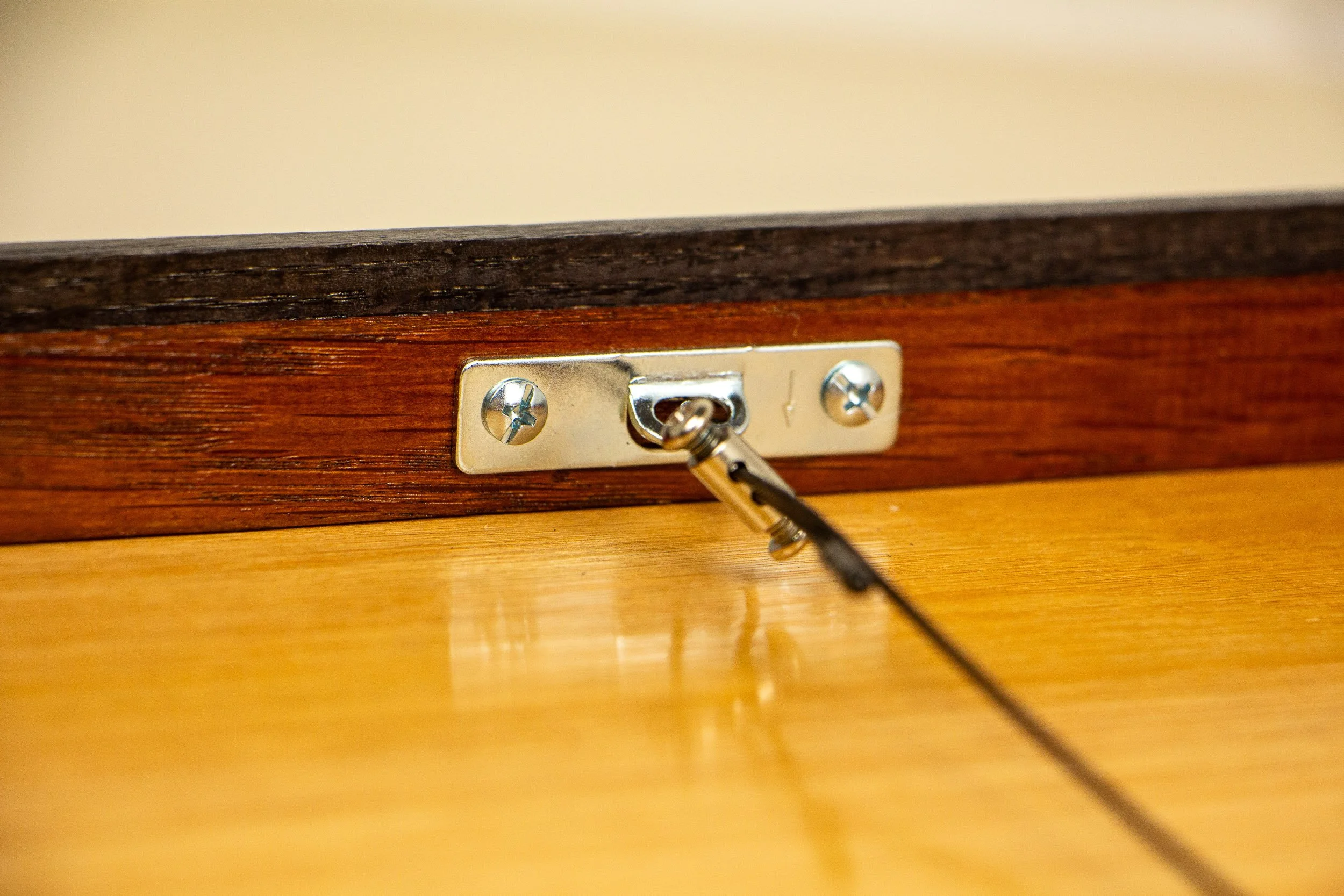 Mêlée of Discovery 003 frame: back detail of the hanging system, focused on the metal plate, cable fitting, and warm-toned backing panel that complete the handmade construction.