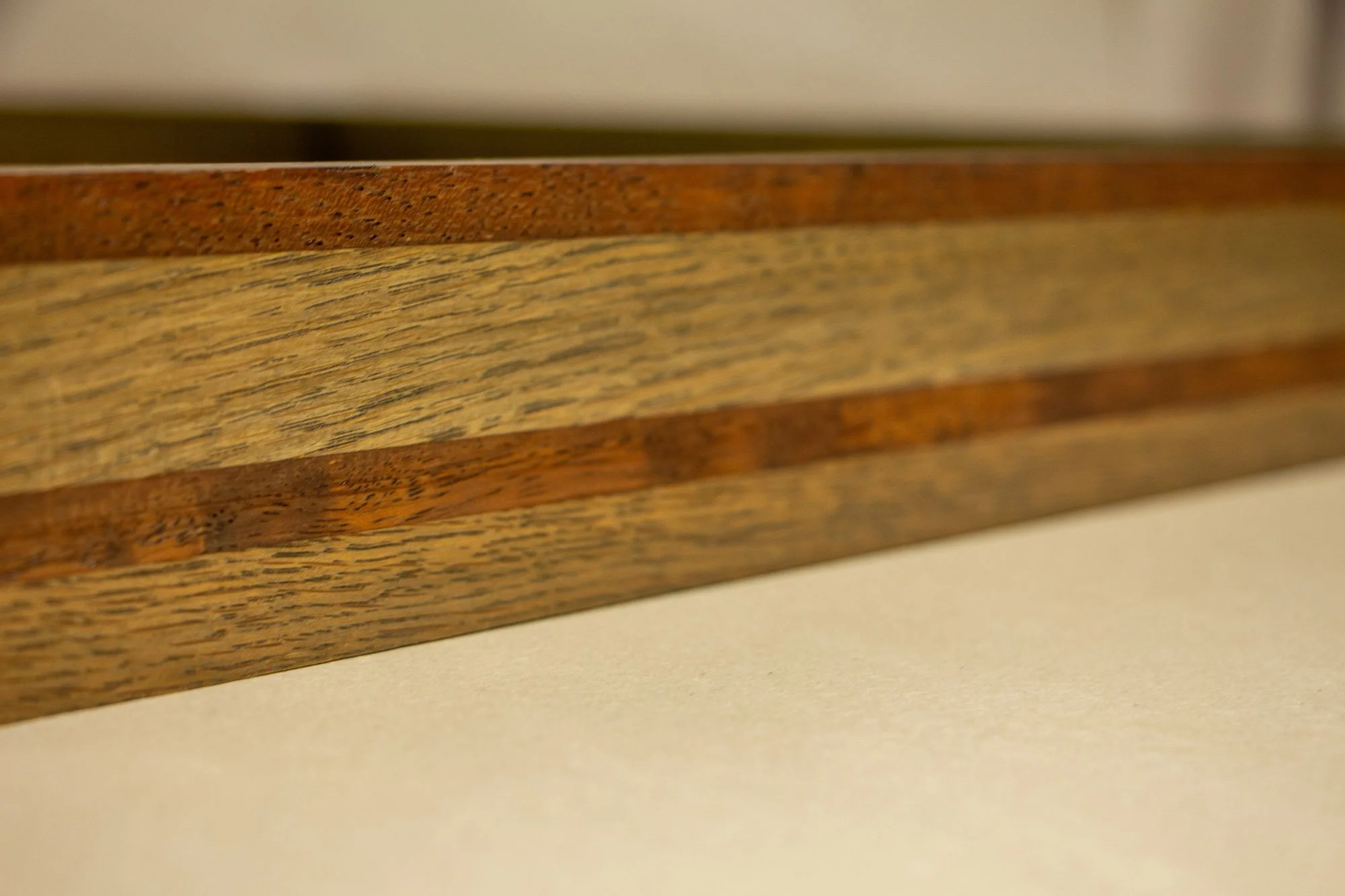 Unseen Signifiers 001 frame detail: angled macro of the frame side, emphasizing the meeting of the darker top strip, the pale oak band, and the darker central inlay. mahogany, oak and beech wood.