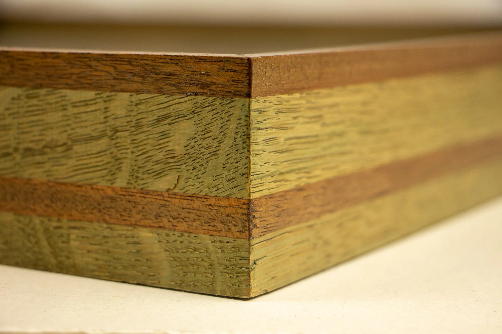 Resonant Syntax 002 frame: close-up of the mitered corner of the layered mahogany-and-oak frame, with a mint, blue, and pink sequence and visible grain across the joined edges