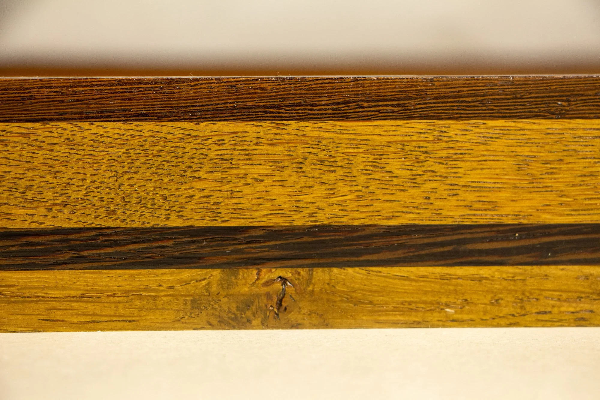 Elusive Cocoon 002 frame: frontal close-up of the side profile with a dark upper rail, bright golden oak-toned band, darker brown central strip, and lower section with diagonal grain detail.