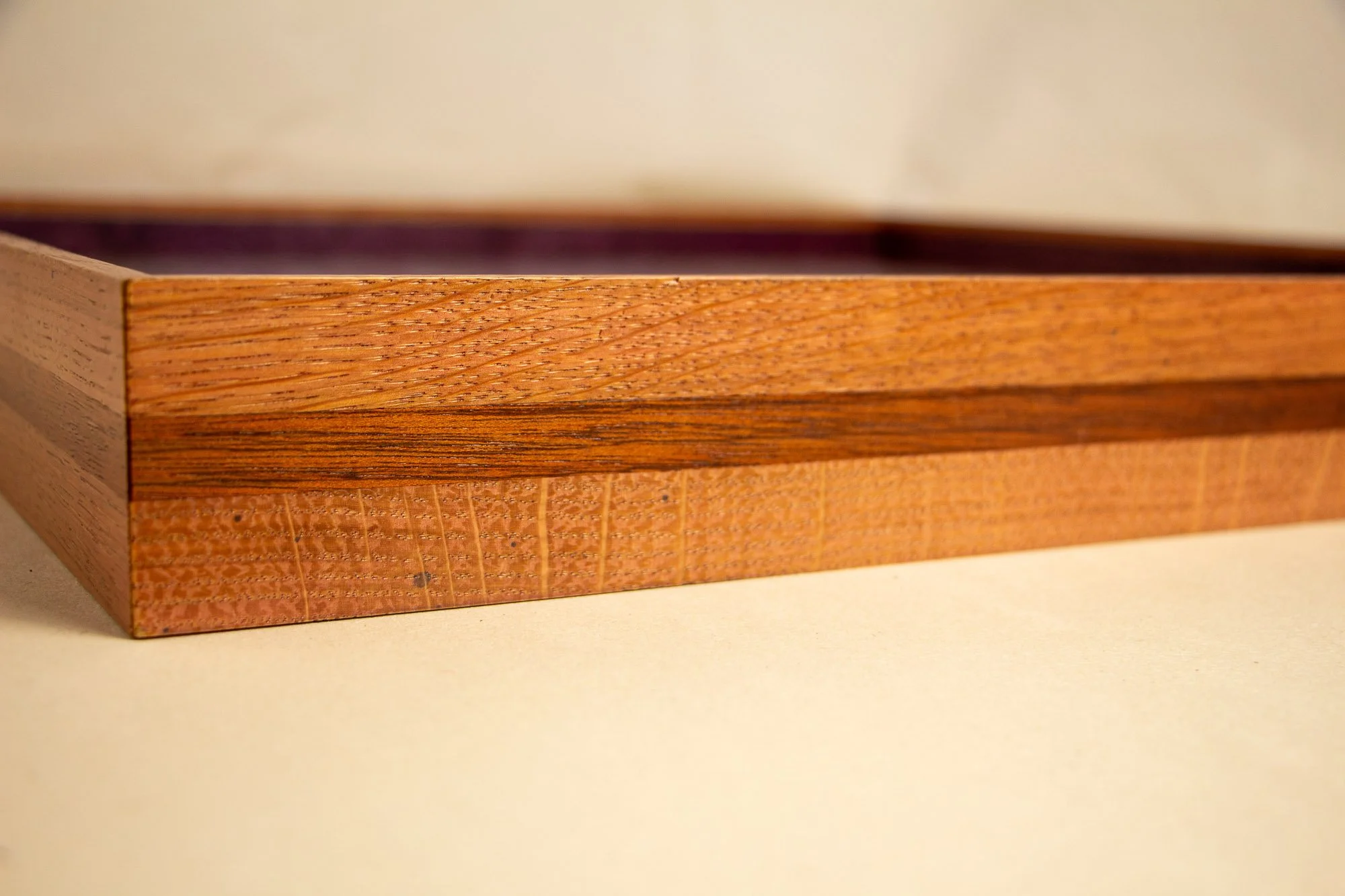 Eclipsing Gravitas 003 frame: side profile detail of the shallow layered frame, showing a warm pink-orange toned oak body, a darker central mahogany band, and the low horizontal construction beneath the glazed artwork.