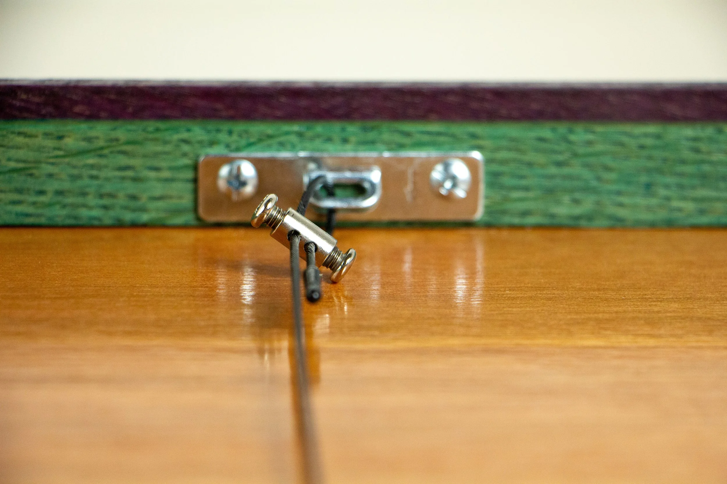 Formless Equation 001 frame: close-up of slotted hanger plate and wire clamp against green inner rail