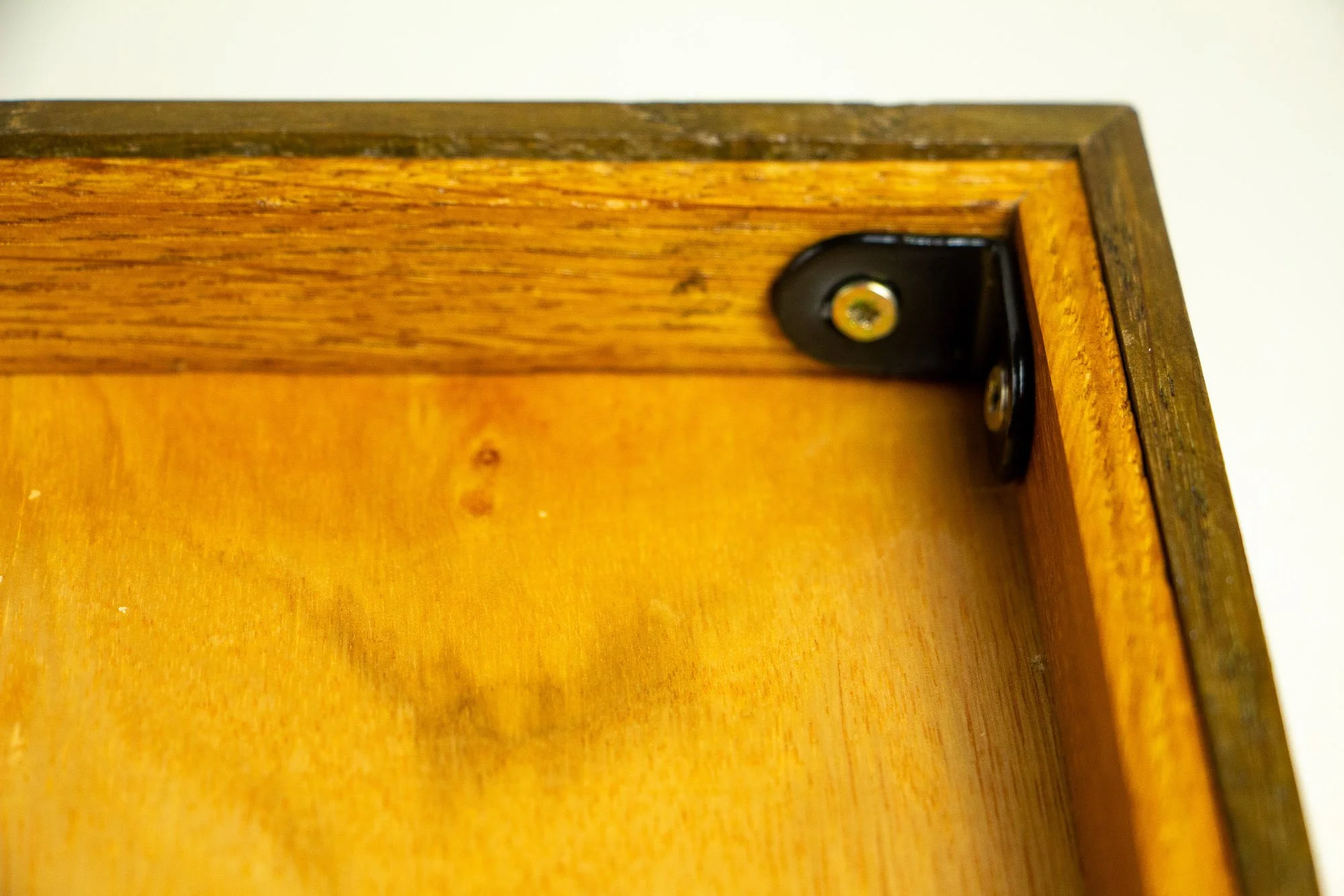 Unseen Signifiers 007 frame detail: close-up of the reverse corner construction, showing the black corner bracket, screw fixing, and the wood grain of the back structure.