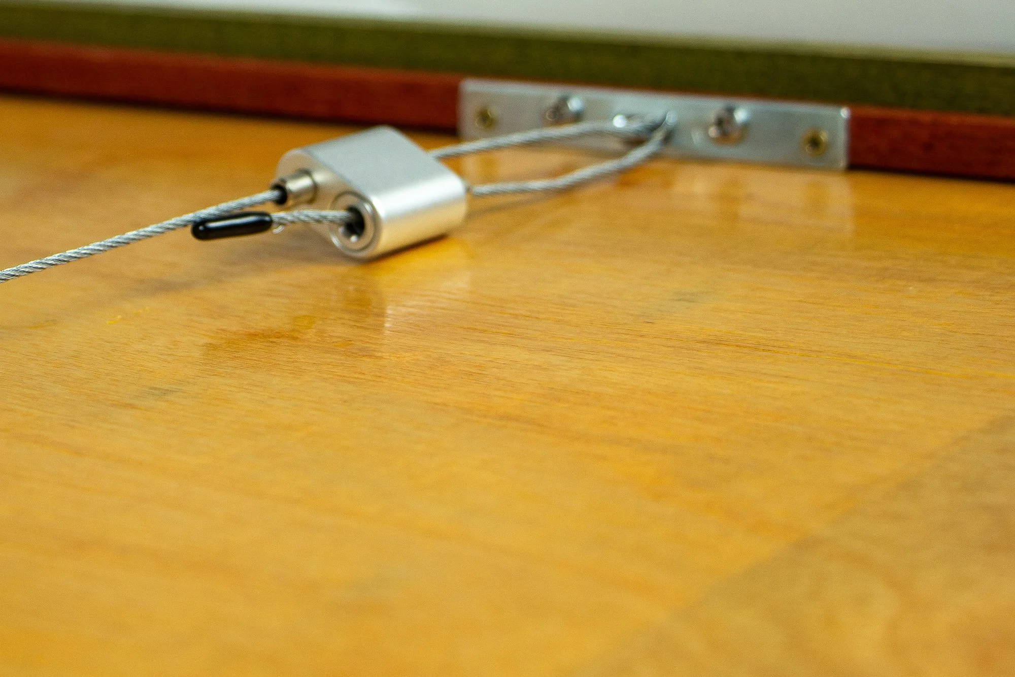 Resonant Syntax 004 frame: reverse detail of the hanging system, with steel cable, silver locking mechanism, metal mounting plate, meranti plywood back panel, and the layered frame construction in green and red-toned bands