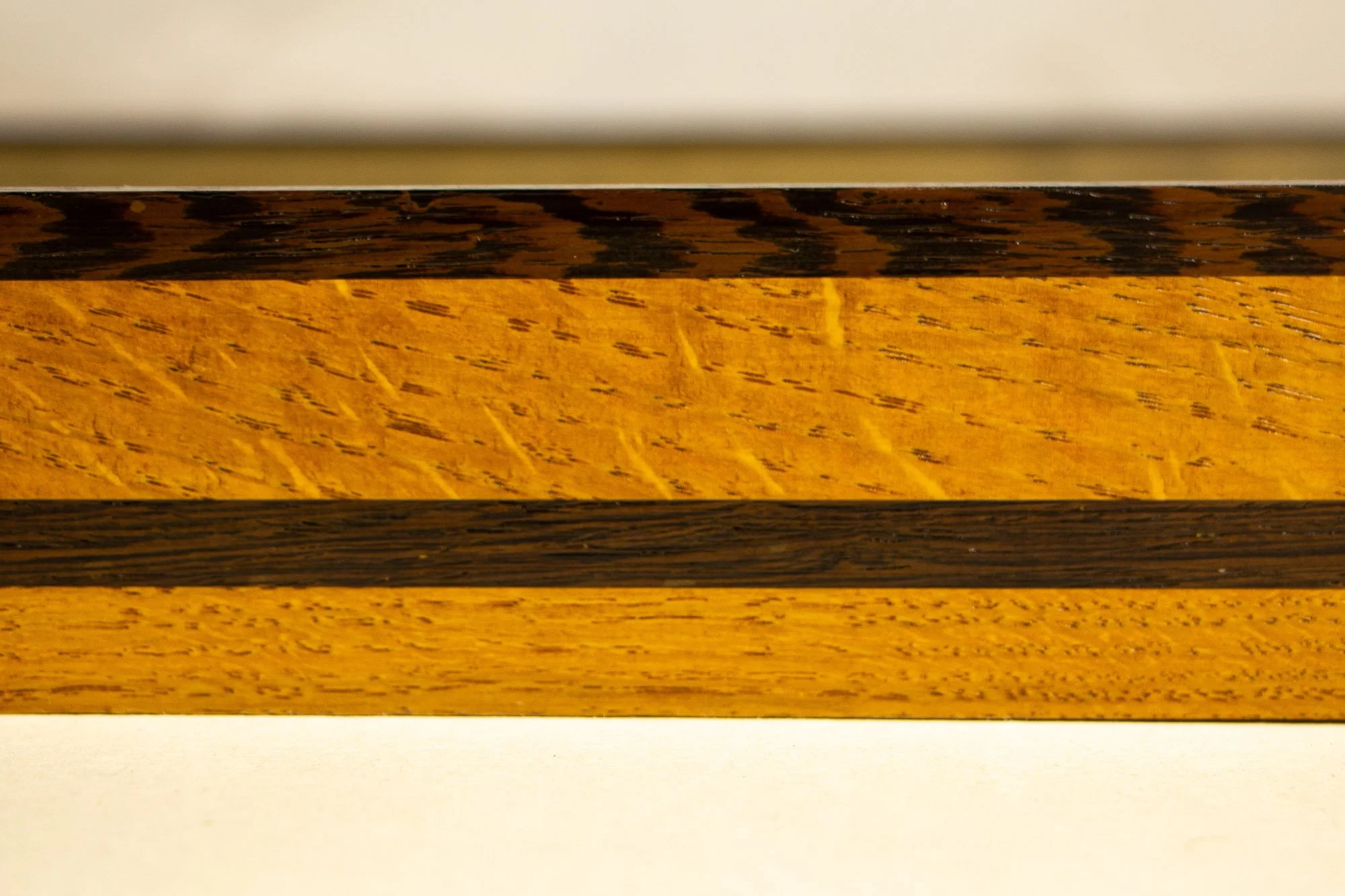 Elusive Cocoon 004 frame: frontal close-up of the layered profile, showing the contrast between the dark wengé top rail and the yellow-toned oak band within the frame’s yellow, blue, and cherry palette.