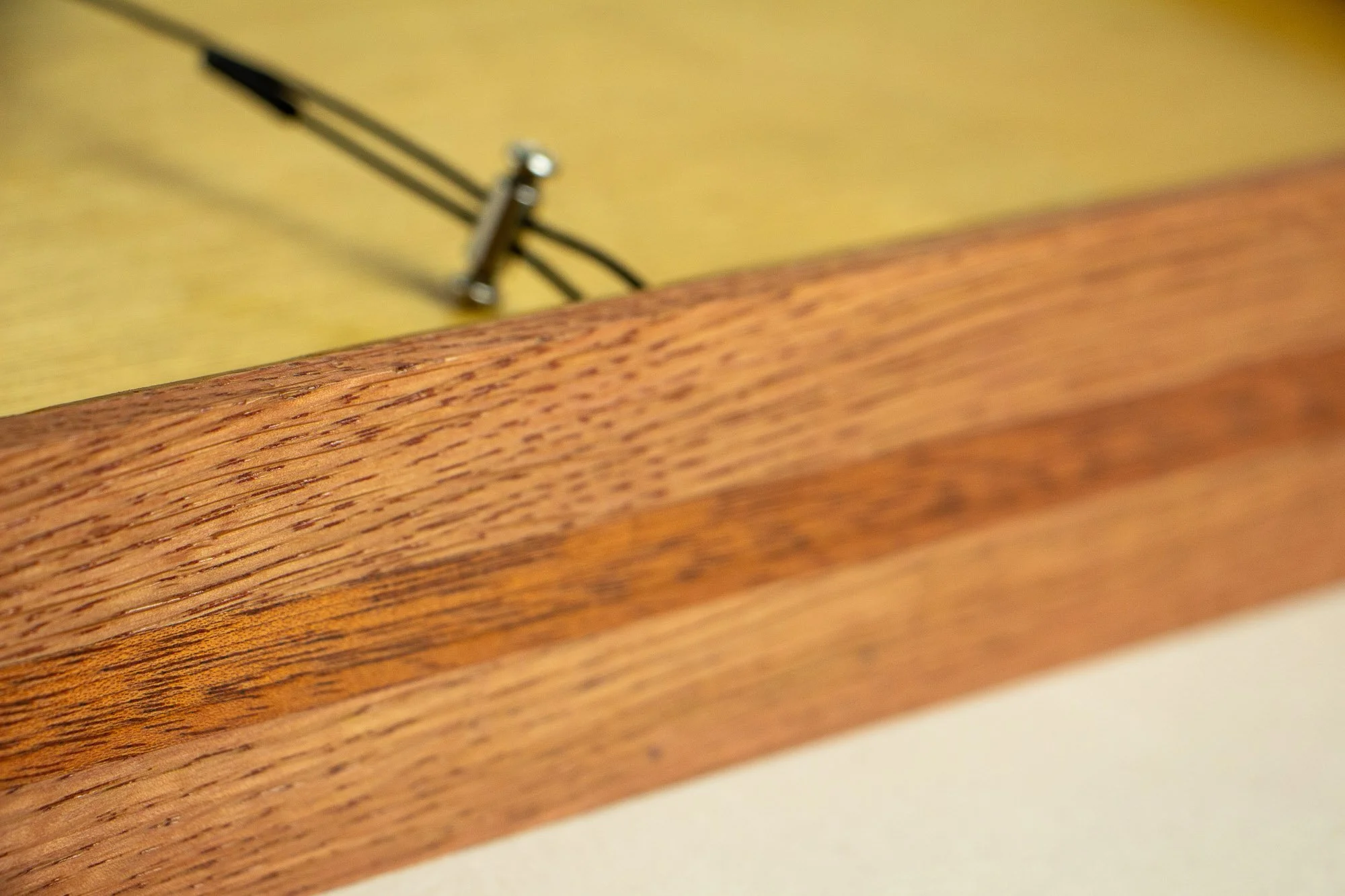 Eclipsing Gravitas 003 frame: rear profile detail of the frame construction, showing the layered warm wood tones and darker central band, with the hanging wire and hardware softly blurred in the background.