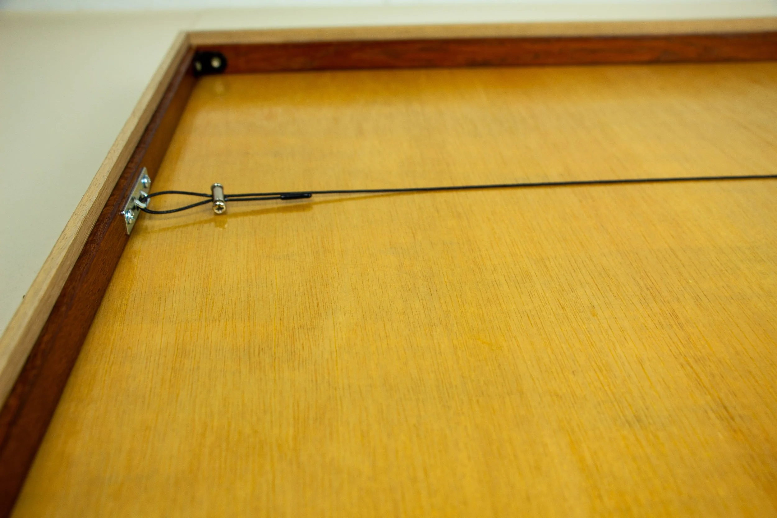 Mêlée of Discovery 004 frame: rear detail of the hanging hardware and wire attachment, mounted against the smooth wooden backing panel.