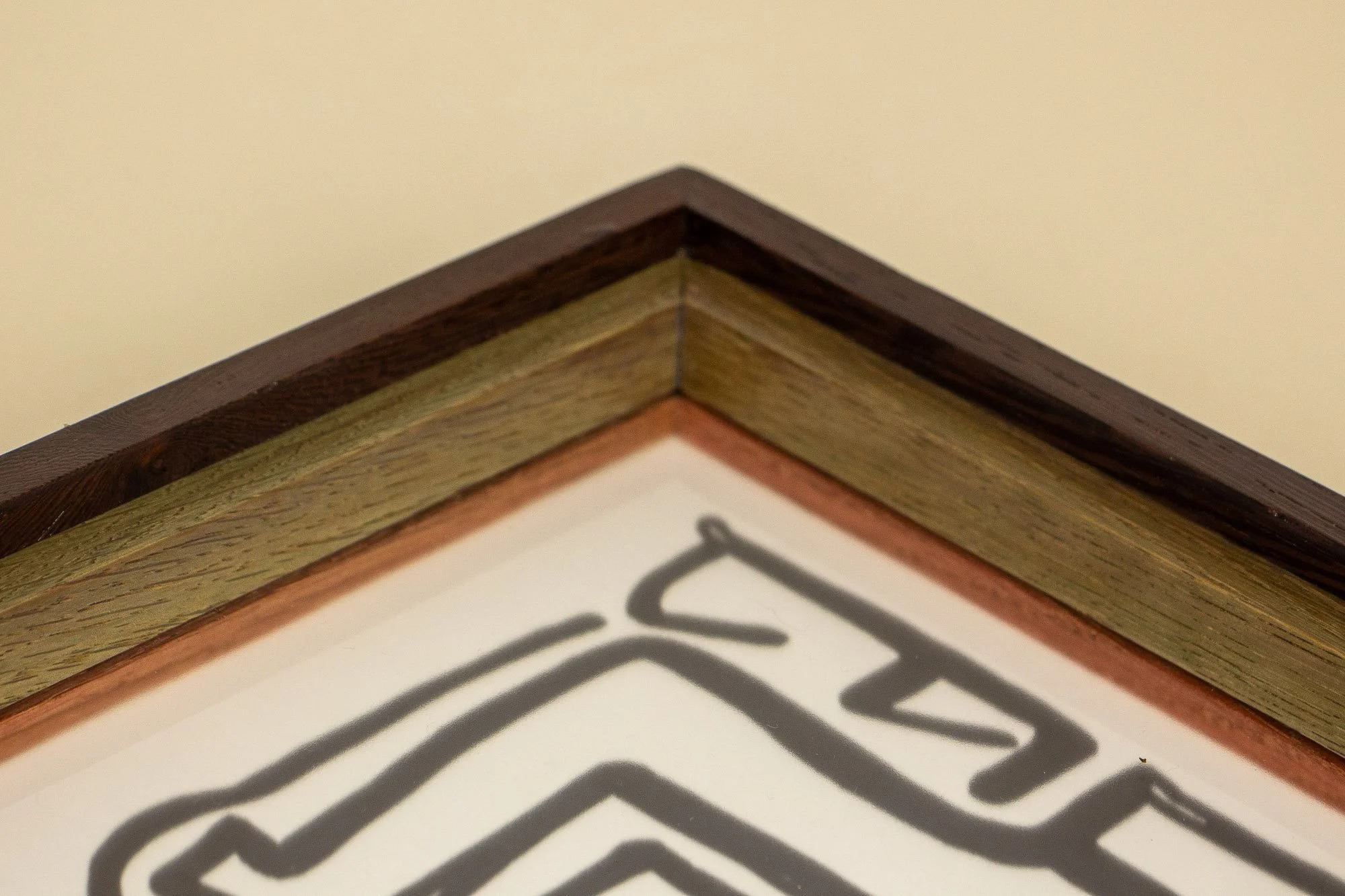 Close-up of the corner of a wooden-framed whiteboard or poster board with black writing, showing the edges of the sign, the border, and the wall behind.