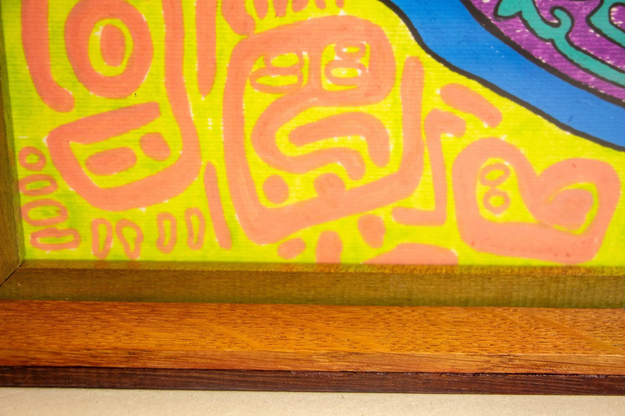 Unseen Signifiers 009 frame detail: front view through the acrylic, showing the lower portion of the frame with warm brown and darker wood bands beneath the artwork’s lime-yellow and pink border. mahogany, oak and beech wood.