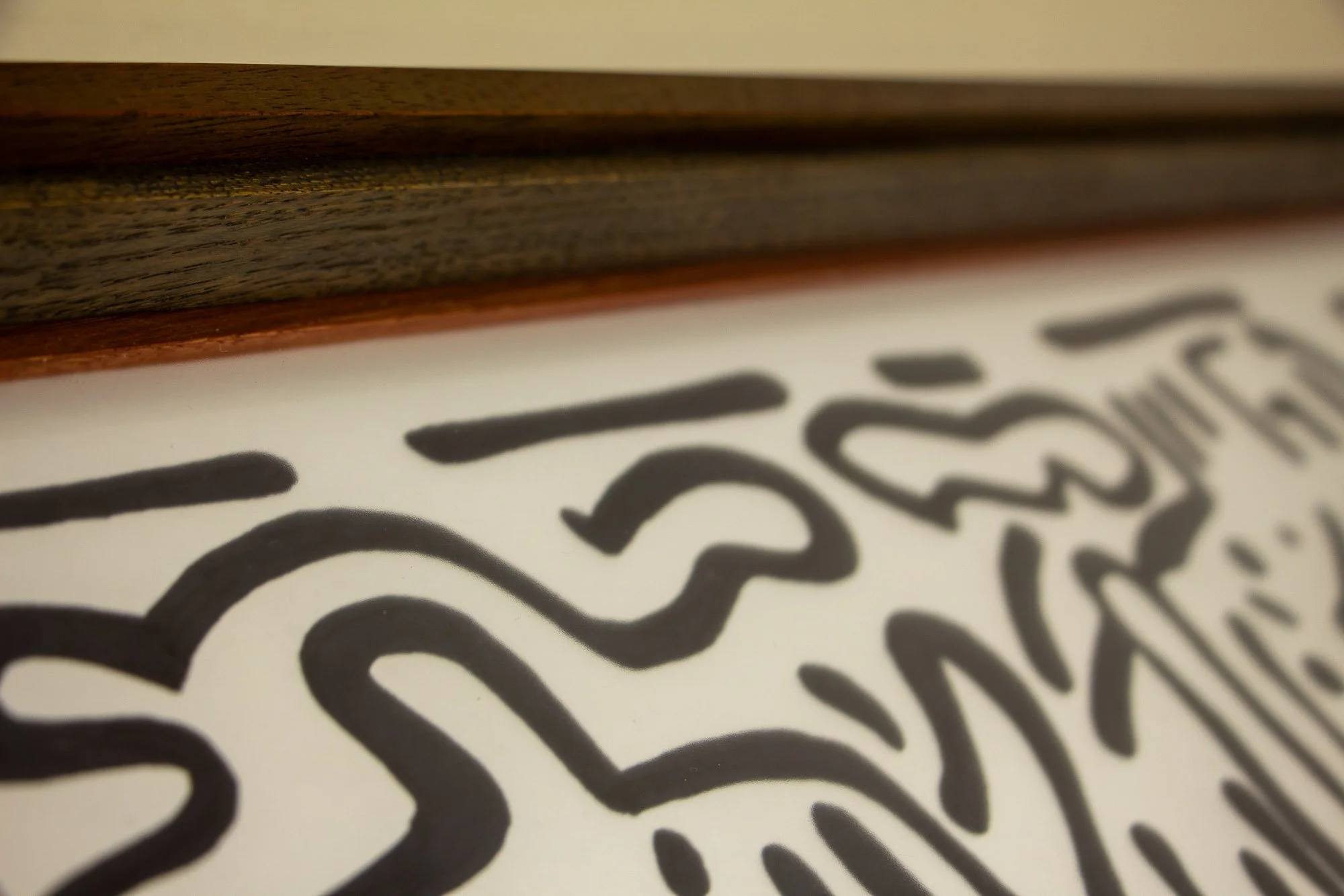 Resonant Syntax 004 frame: low angled close-up along the inner frame edge, with dark green-toned oak beside a narrow red inner lip, the artwork visible beneath the glass