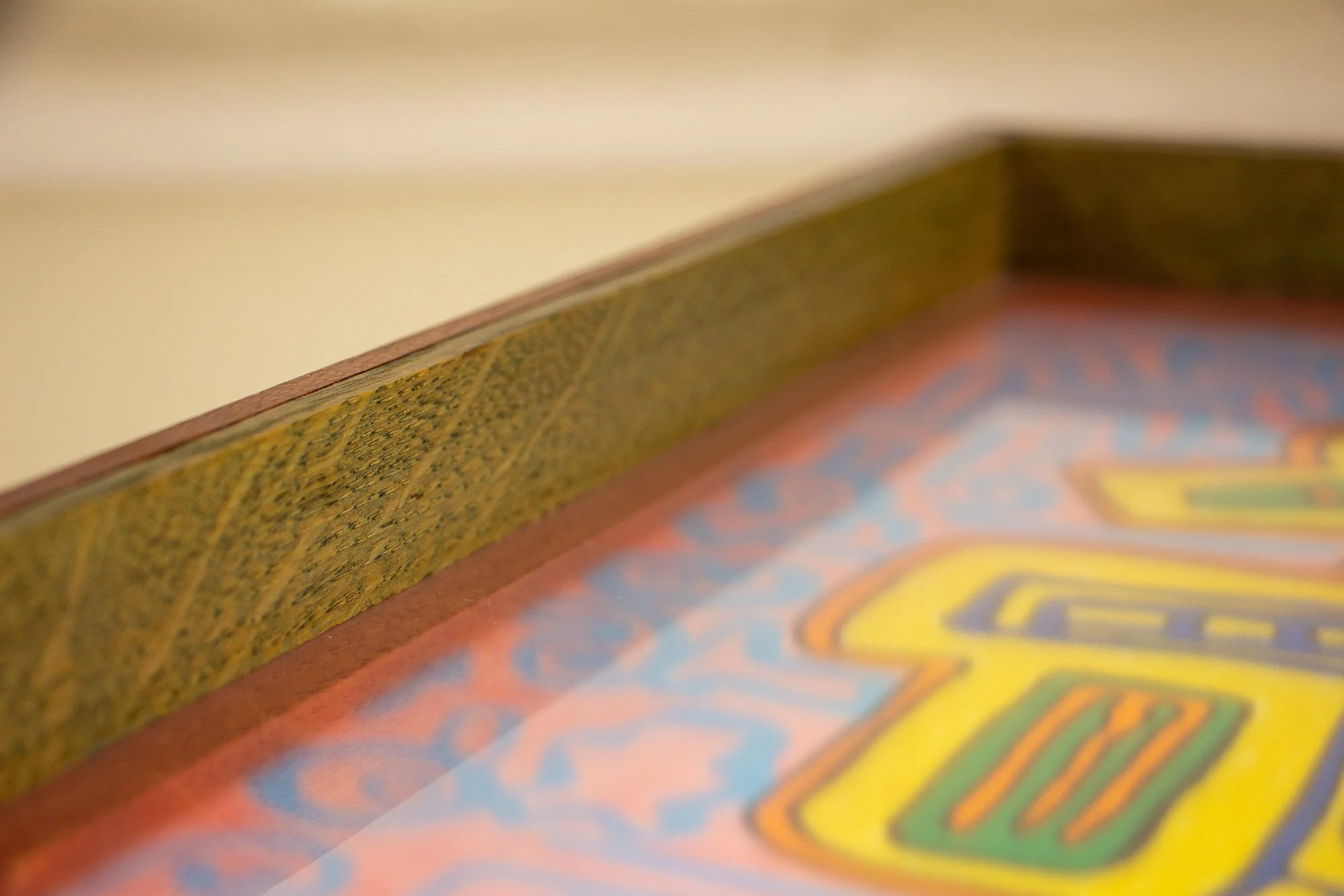 Unseen Signifiers 006 frame detail: angled close-up of the olive-green inner liner and reddish-brown outer rim, with the glass surface softly reflecting the pink and blue artwork beneath. mahogany, oak and beech wood.