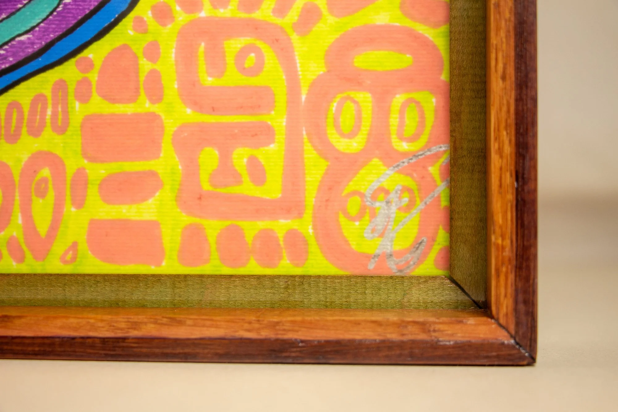 Unseen Signifiers 009 frame detail: close-up through the acrylic of the lower right corner, showing the silver signature over the lime-yellow field with soft pink symbols, bordered by the layered wooden frame. mahogany, oak and beech wood.