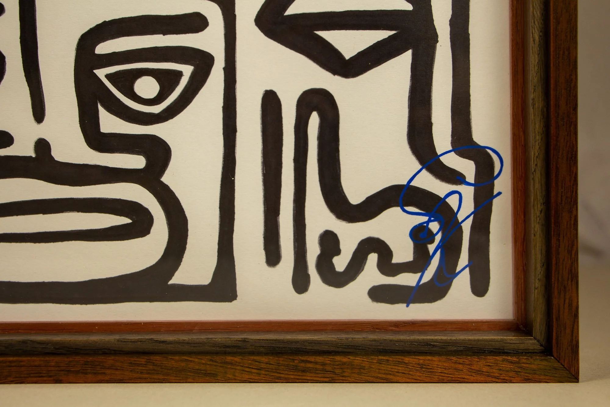 Resonant Syntax 004 frame: lower-right corner detail showing the blue signature on paper, bordered by the red inner lip, dark green-brown inner oak band, and granada-red outer frame