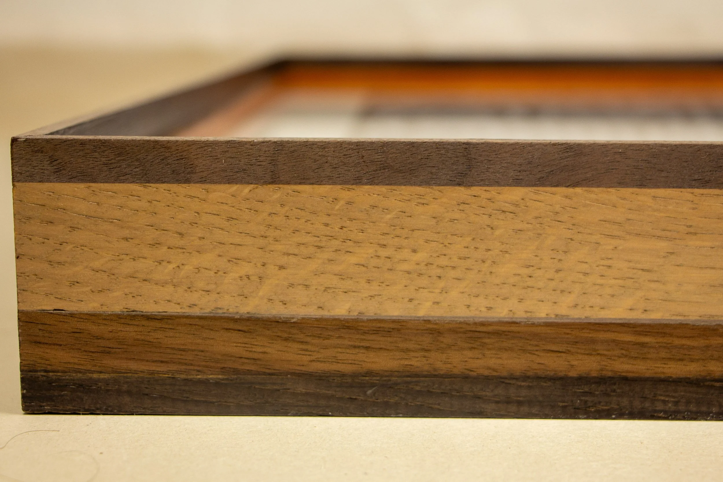 Mêlée of Discovery 001 frame: close side profile of the frame, showing the layered alternation of darker and lighter wood bands and the clean, restrained front edge.