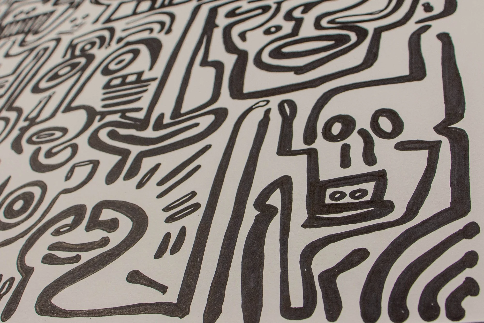 Veiled Alchemist 001 detail: angled close-up of a skull-like face beside an elongated rectangular figure, showing bold black contours, repeated oval forms, and radiating marks across the white surface.