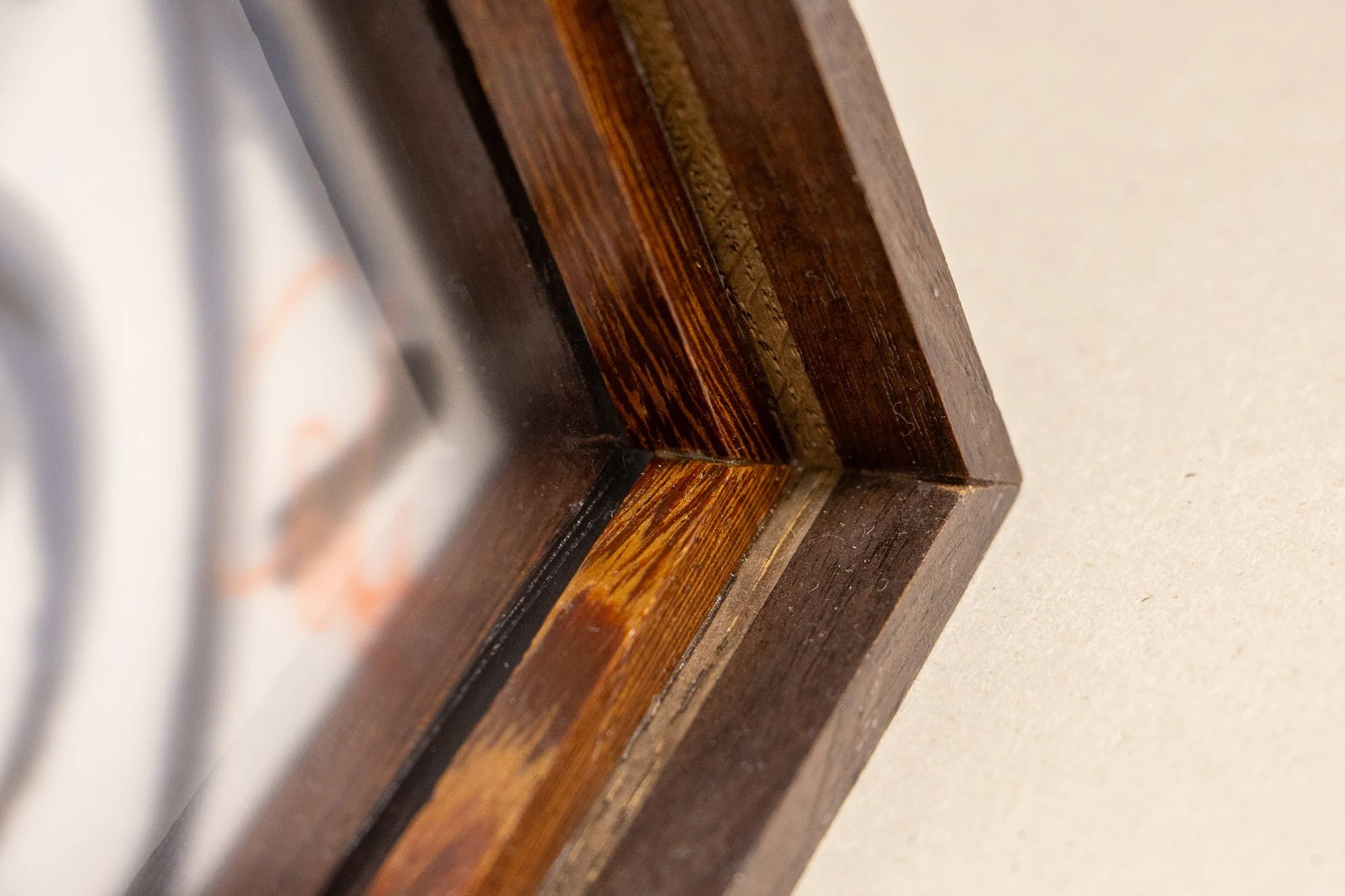 Luminous Parallax 001 frame: low oblique view along the frame edge, showing the long receding profile, subtle shifts between dark and muted wood surfaces, and the understated depth of the construction.