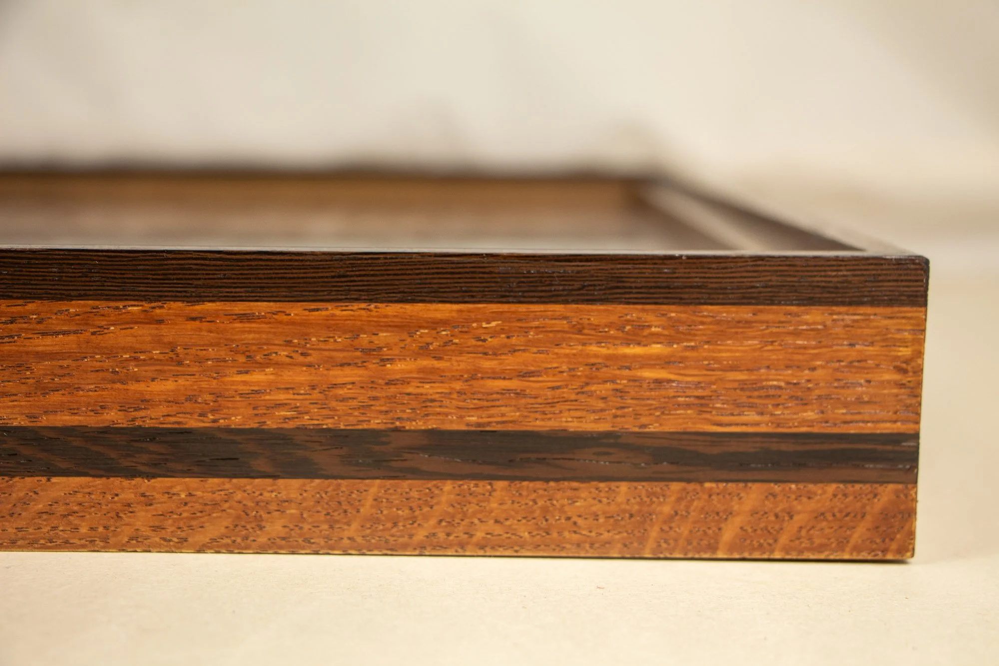 Elusive Cocoon 001 frame: angled side view of the elongated frame construction, emphasizing the layered profile, visible grain, and the tonal rhythm between the dark outer edge and lighter ash-toned band.