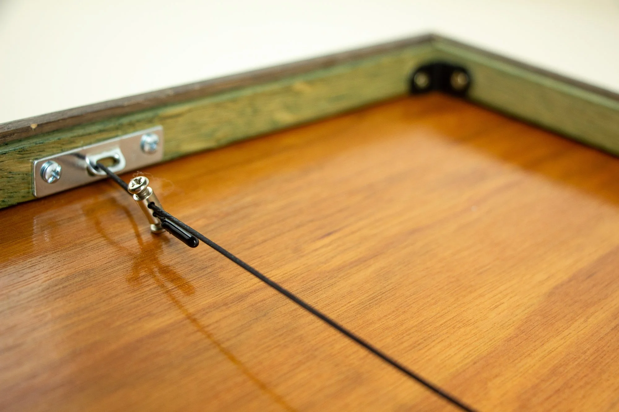 Luminous Parallax 004 frame: reverse-side detail of the hanging system, featuring metal bracket hardware and tensioned steel cable against the warm-toned wooden back panel.