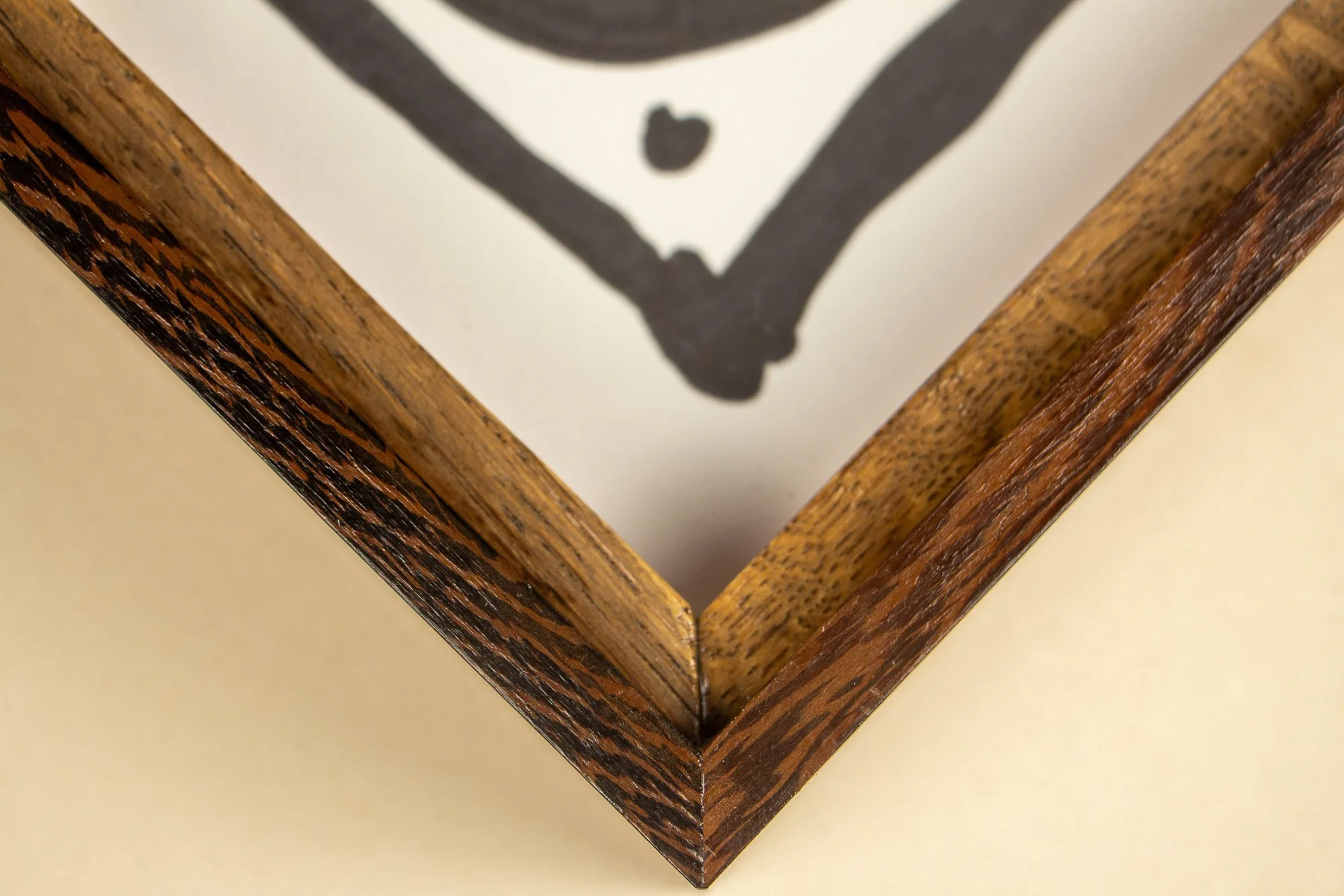 Close-up view of the corner of a picture frame with a dark brown wood grain finish, with part of the artwork visible inside.