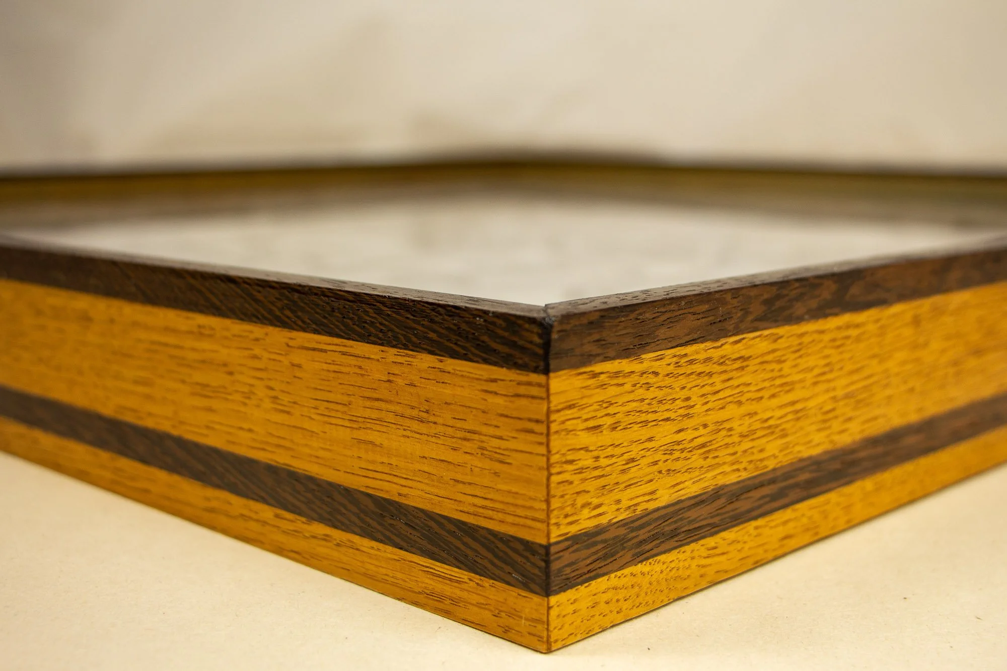 Elusive Cocoon 004 frame: mitered front-corner close-up of the layered wengé-and-oak frame, combining yellow-toned oak with dark wengé bands in a crisp angular construction around the artwork.