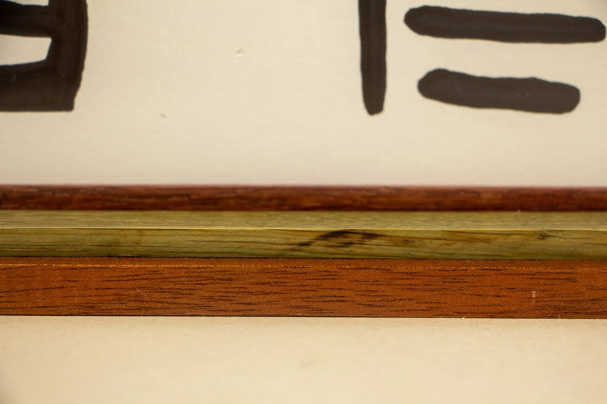 Resonant Syntax 001 frame: lower edge detail of the frame construction, with layered mahogany and oak bands, inner spacer, and the artwork surface visible above