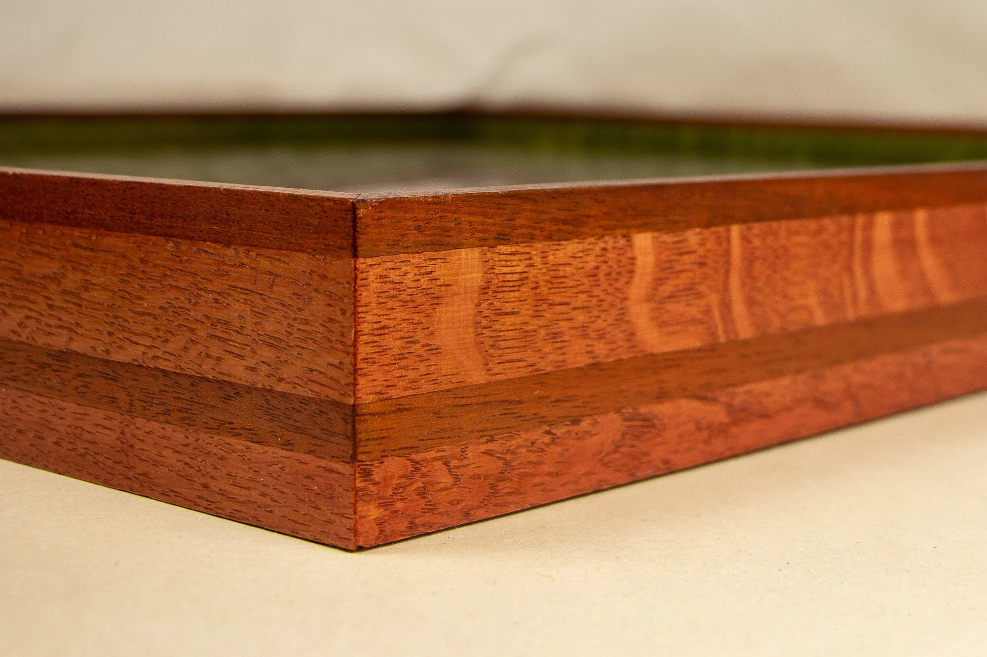 Resonant Syntax 003 frame: angled close-up of the frame edge, showing the red outer band, vivid green inner spacer, dark granada lip, and the artwork surface beneath the glass