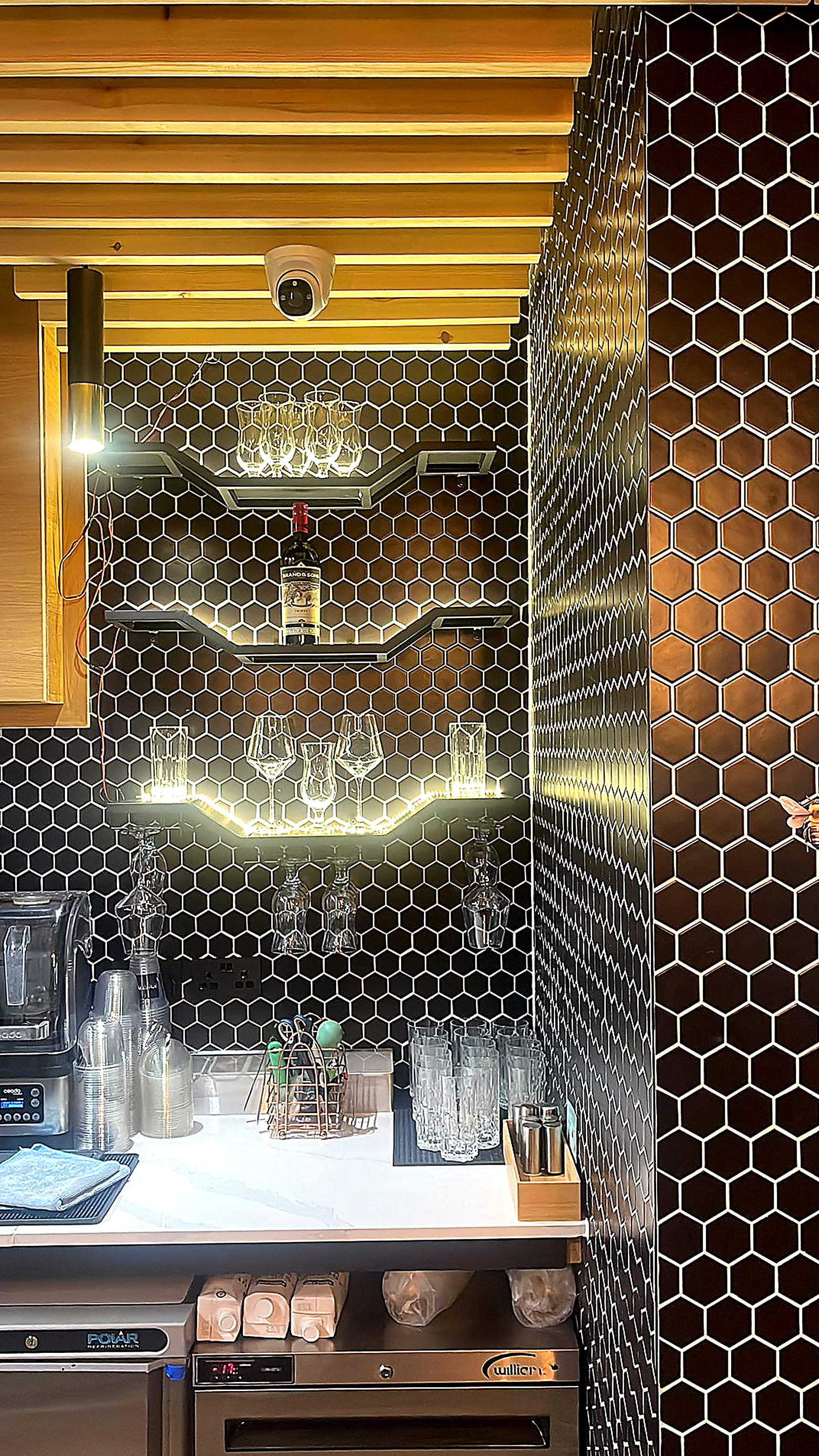 Bar back — black hex-tile feature wall and backlit floating shelves for the stemware programme.