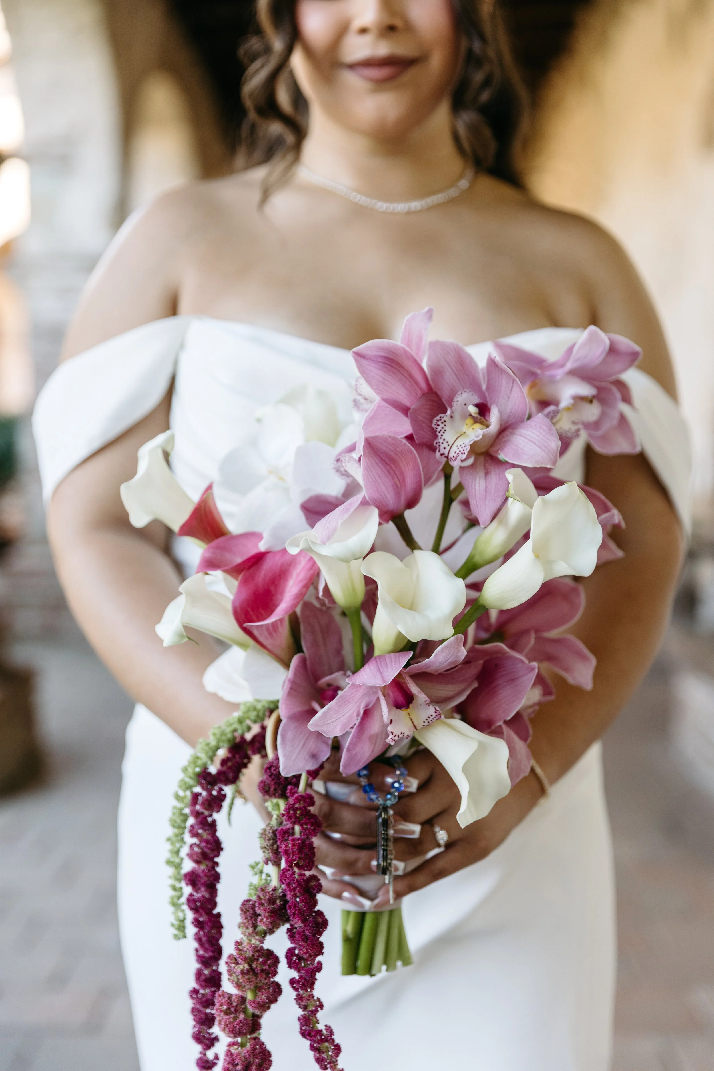 A woman dressed in white holding a bouquet of pink and white orchids and purple amaranthus flowers.