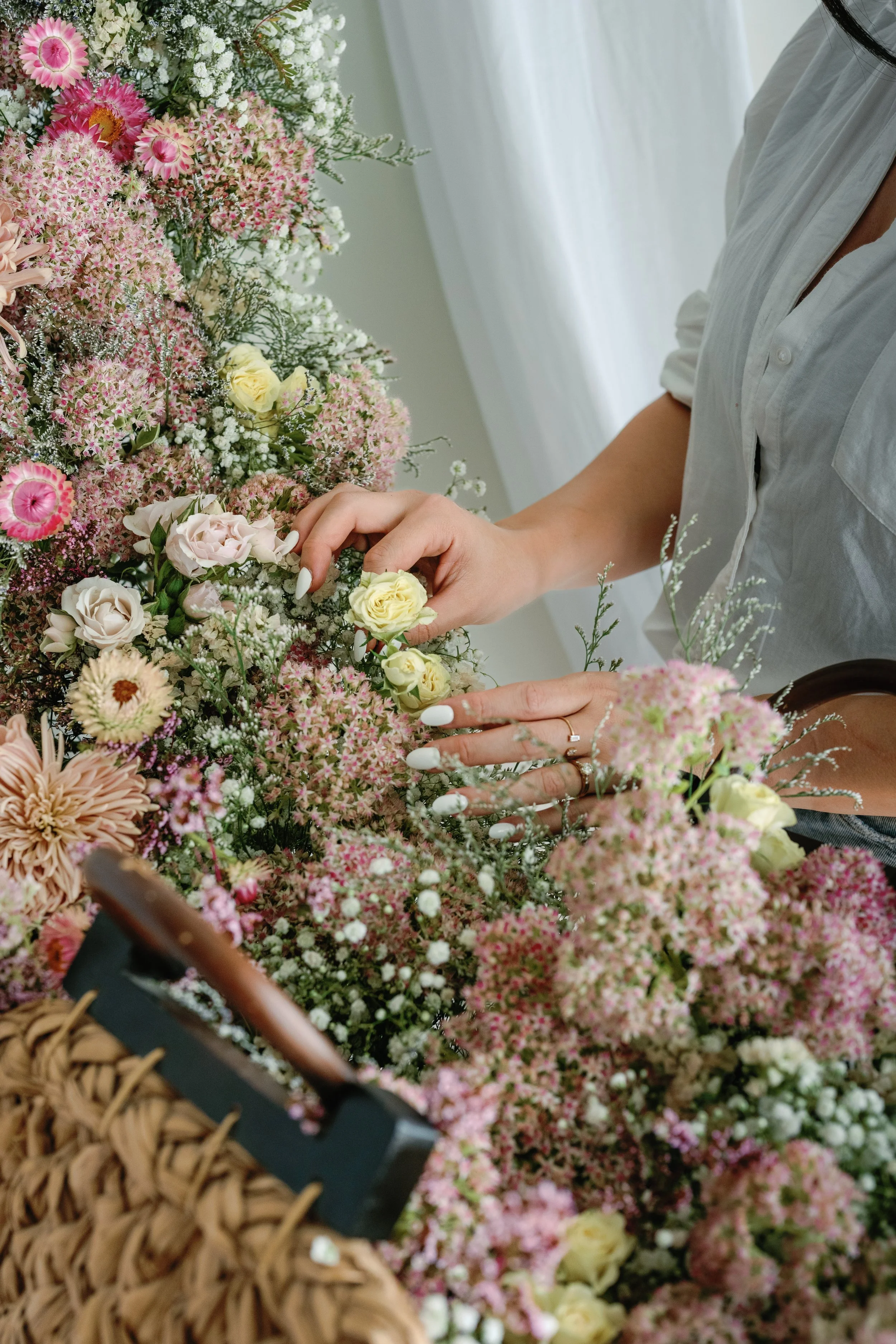 Person arranging a large bouquet of pink, white, and yellow flowers on a table.