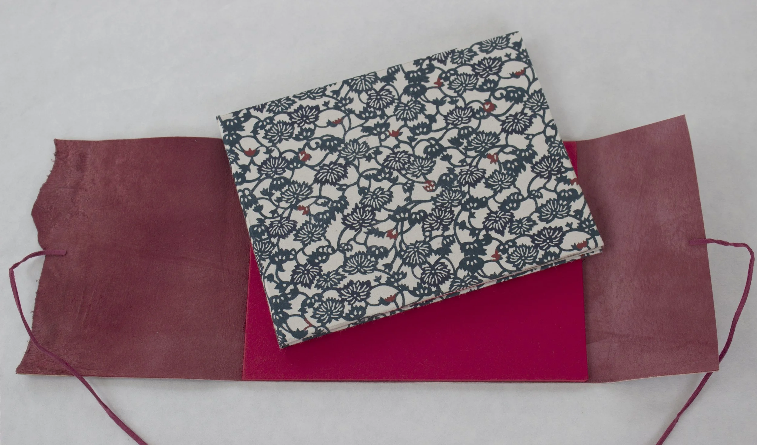 Decorative box with a black and white floral pattern, resting on red and pink paper, with a pink ribbon attached.