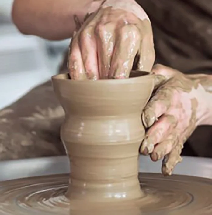 Person shaping wet clay on a pottery wheel with their hands.