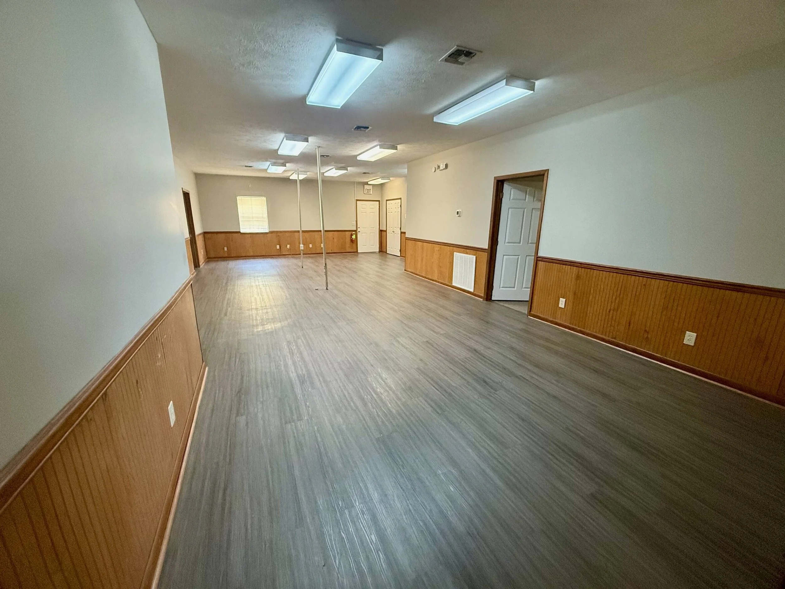 Empty room with wooden wainscoting, hardwood flooring, ceiling lights, and a pole in the center.