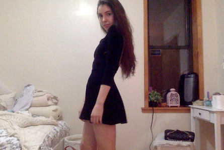 A young woman with long dark hair standing in a bedroom.