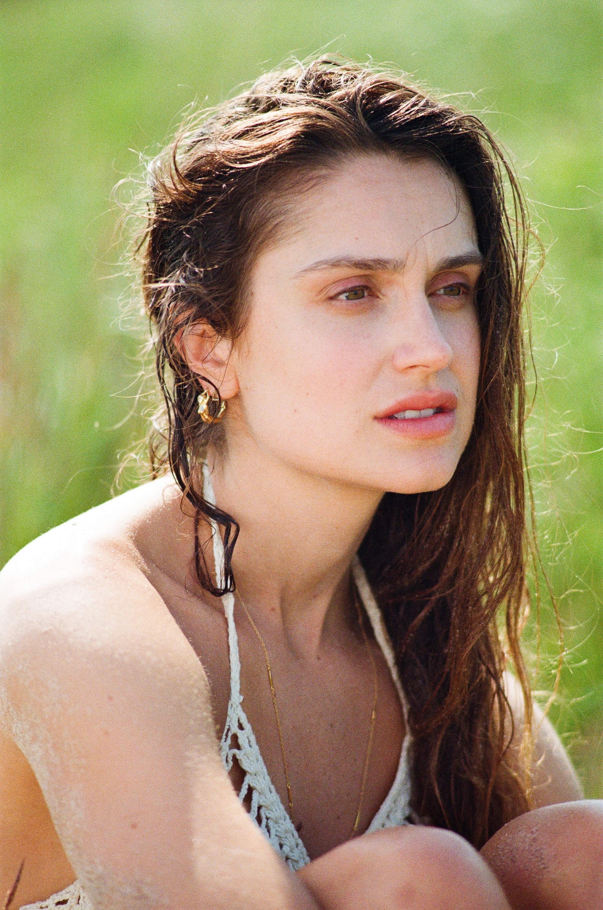 A young woman with wet hair and light skin looking carefully to the side, outdoors against a green background. Photo edited by Mary Perrino.
