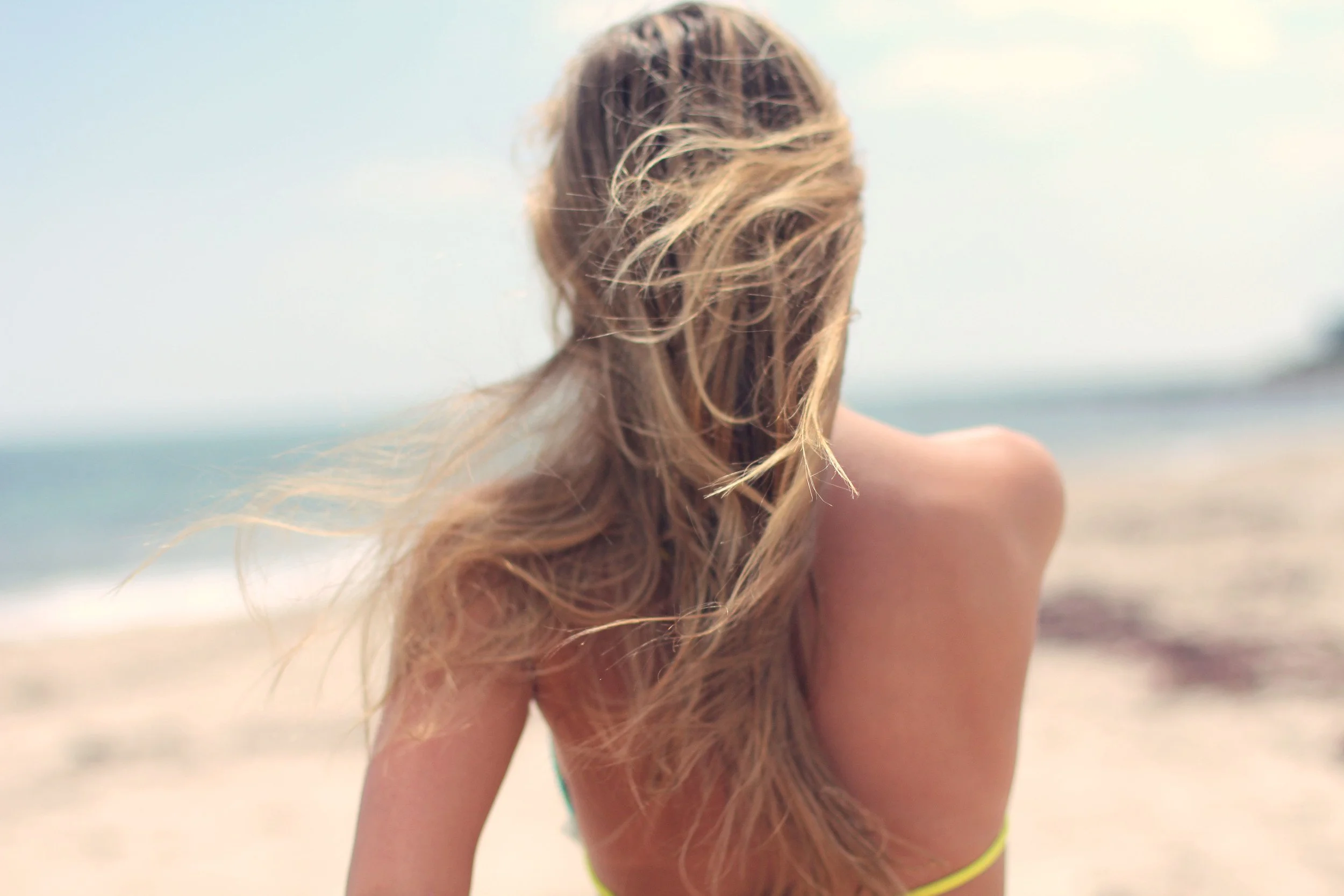 A woman with long, wavy blonde hair looking away on a beach.