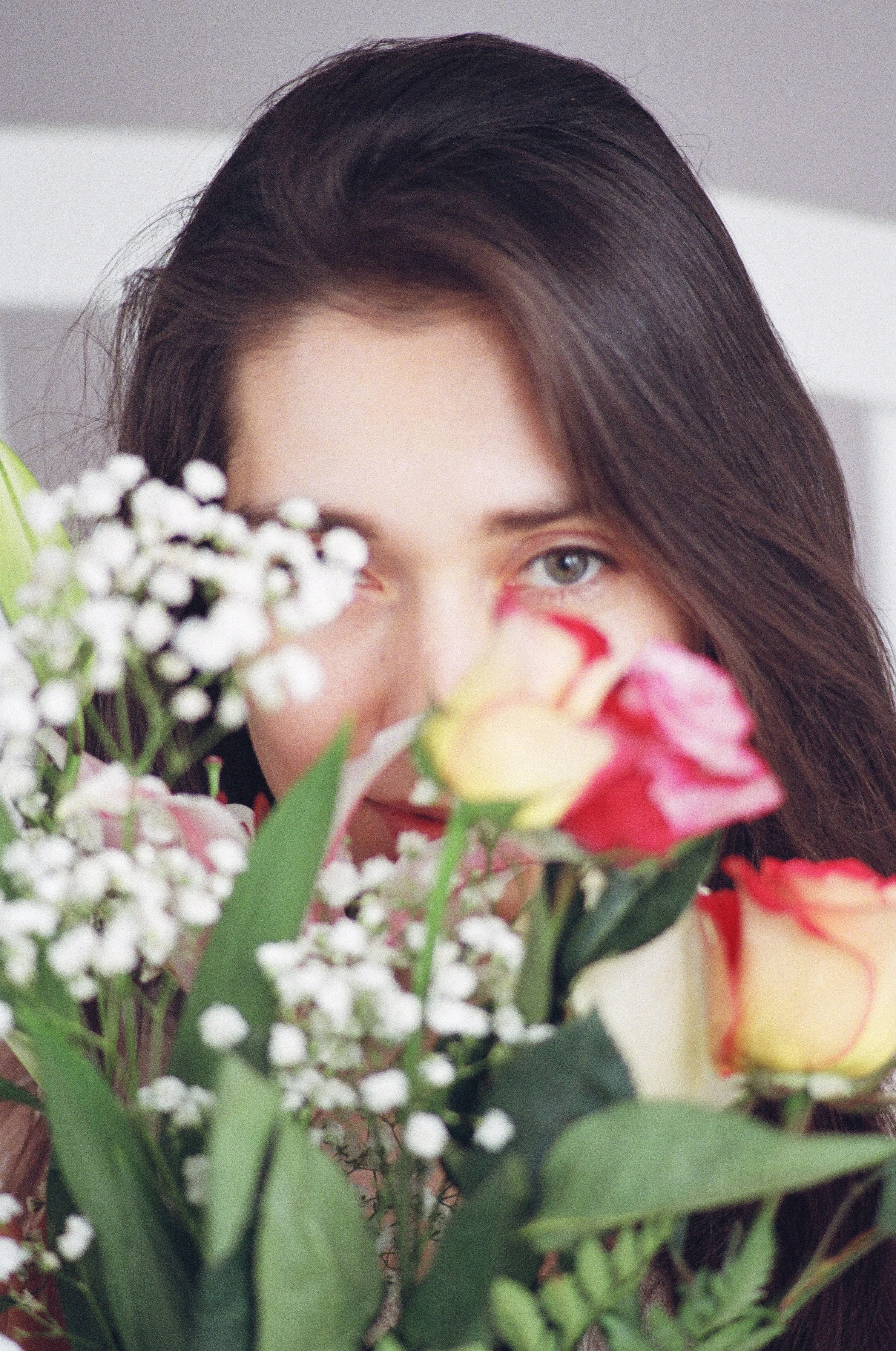 A woman with long dark hair peeking through a bouquet of colorful roses and small white flowers.