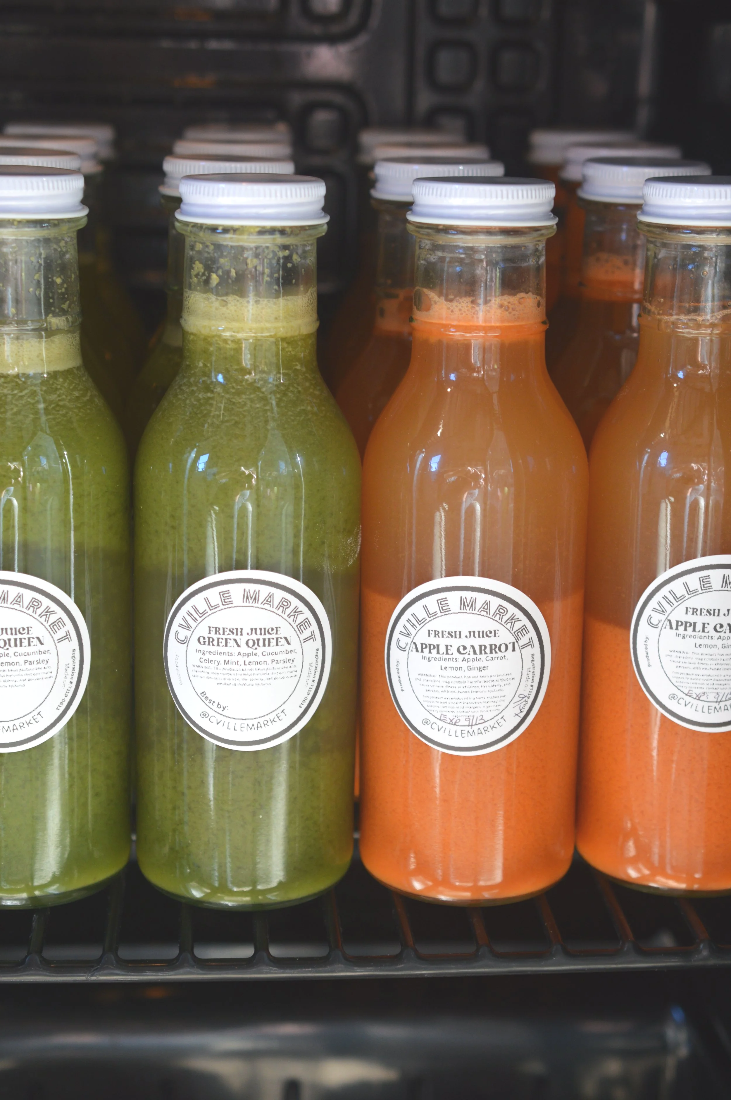Bottles of fresh juice on a shelf, with labels indicating flavors such as Green Queen and Apple Carrot.